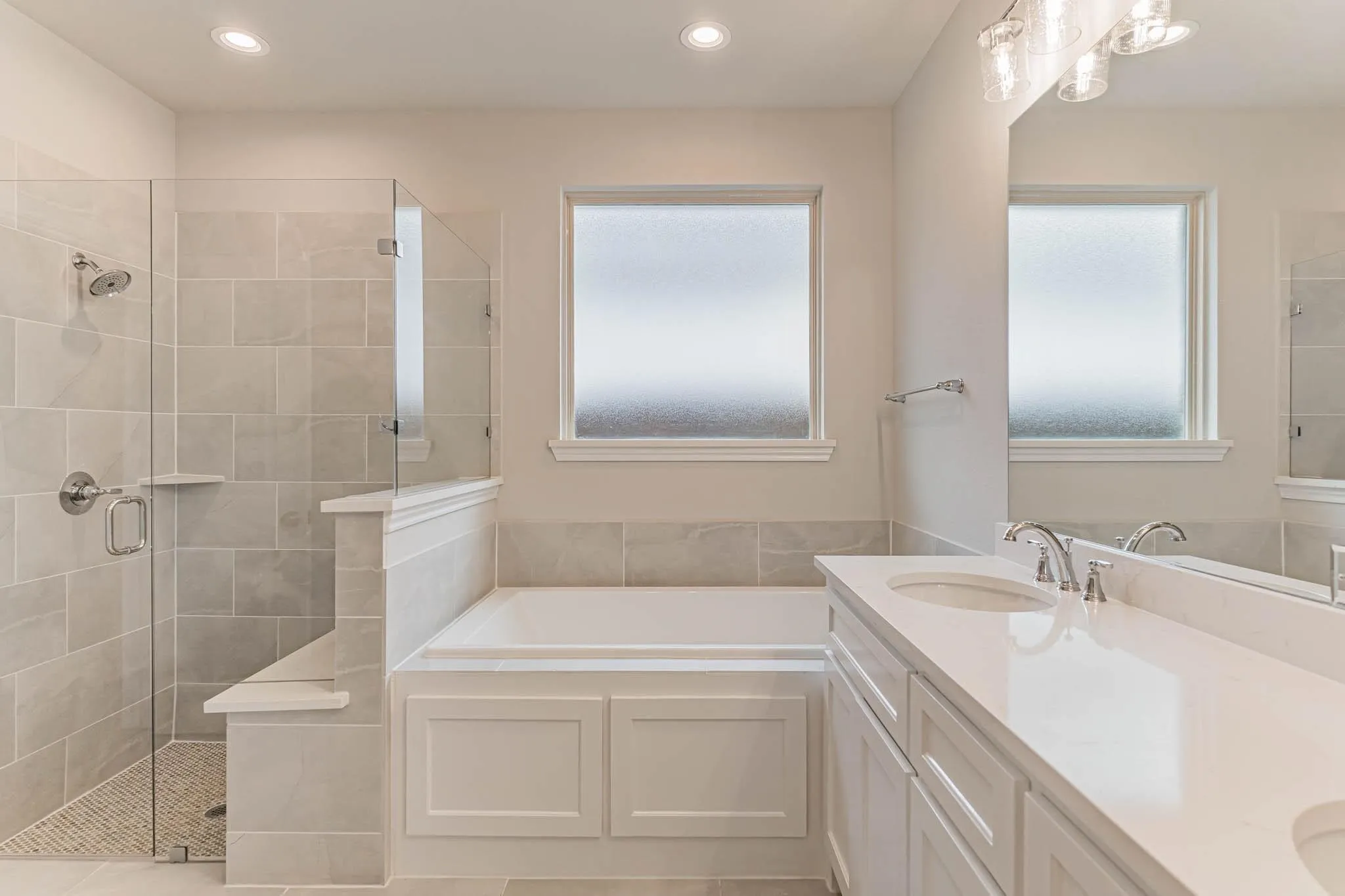 Spacious bathroom featuring a glass-enclosed shower, built-in bathtub, dual vanity with undermount sinks, and a large mirror