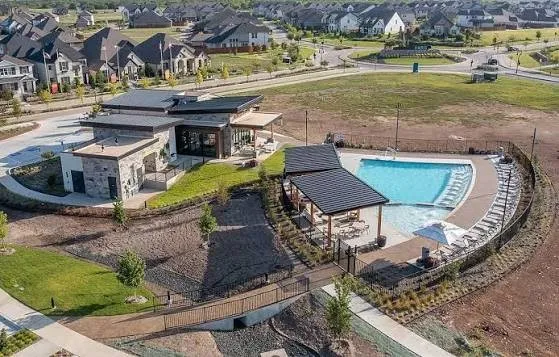 Community pool with an integrated lounge area, adjacent covered patio, and a separate stone-clad clubhouse structure