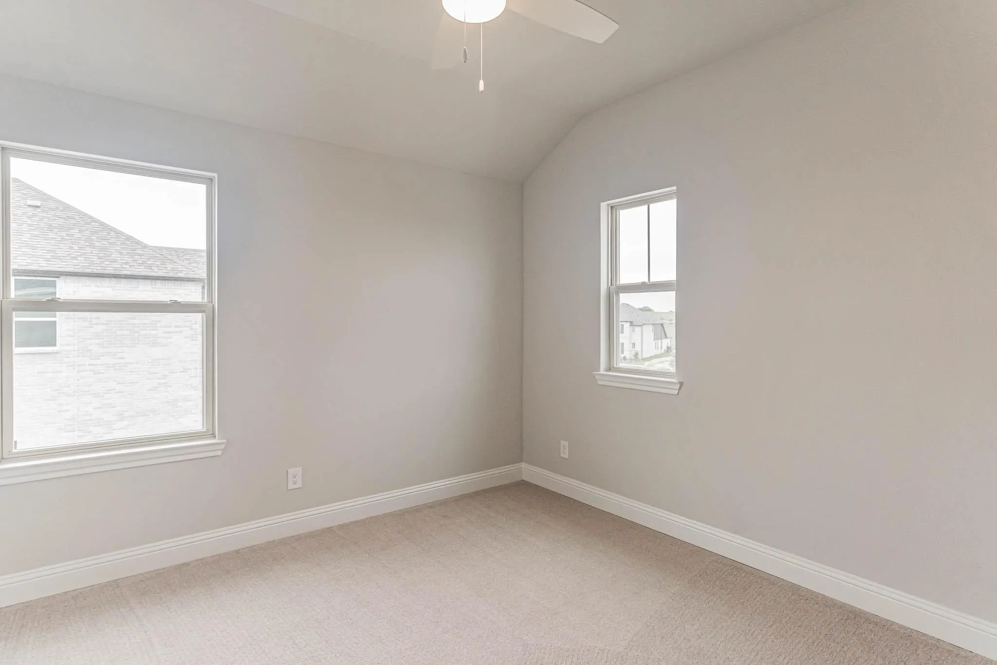 Vaulted ceiling, two windows, ceiling fan, neutral wall tones, and plush carpet