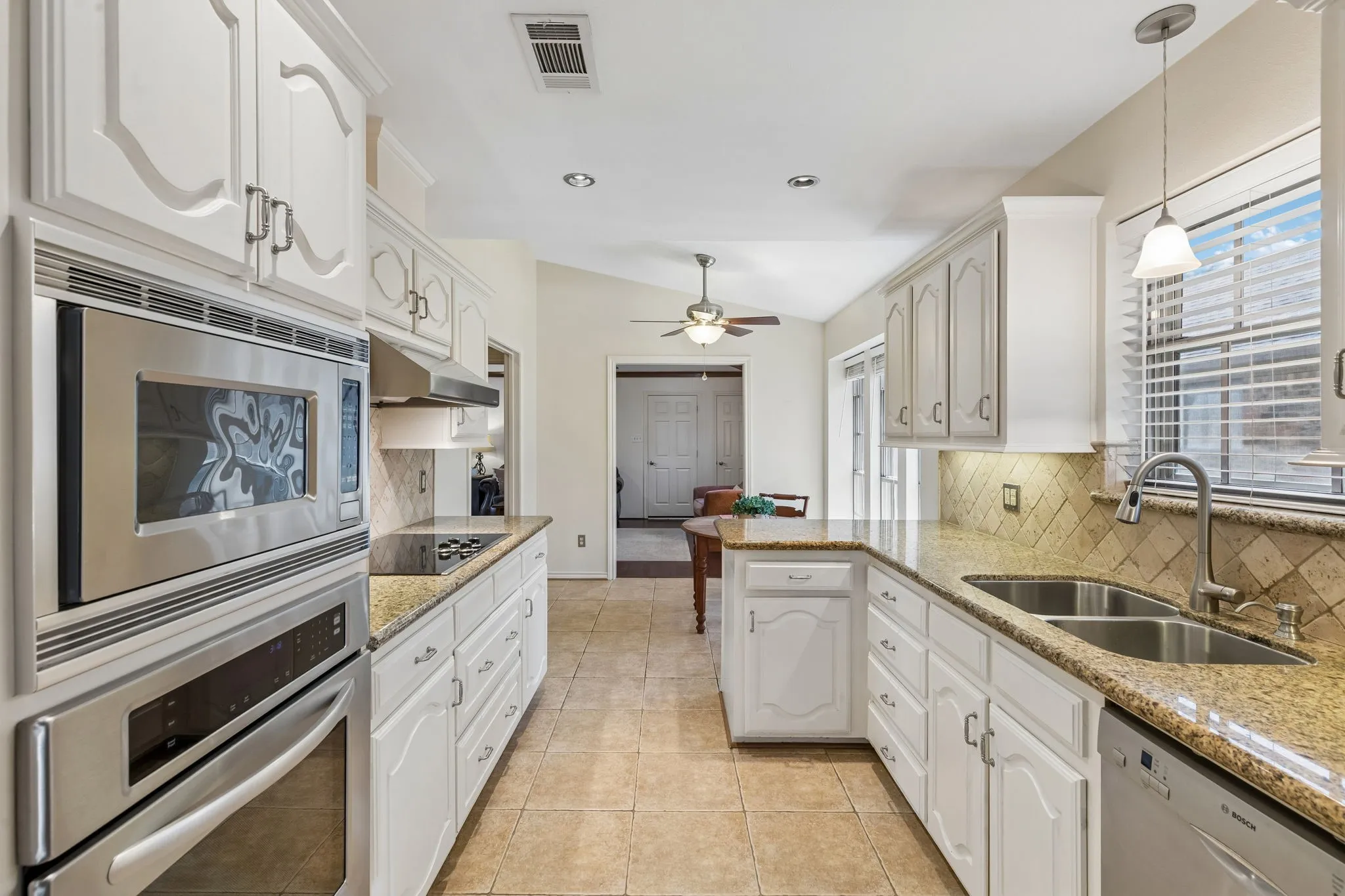 Kitchen featuring white cabinetry, stainless steel appliances, granite countertops, tile flooring, and a double basin sink