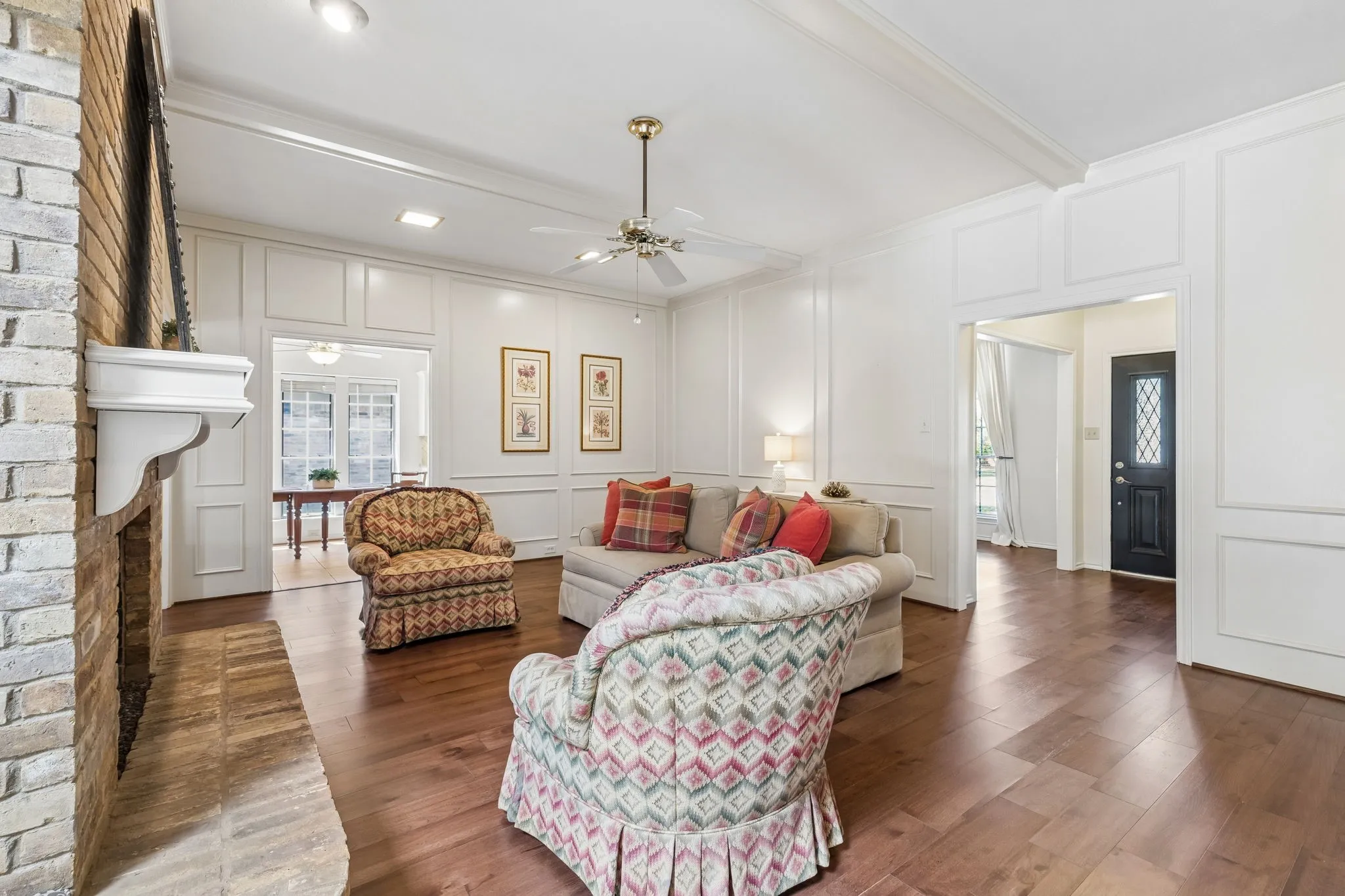 Brick fireplace with a white mantel, wood-finish flooring, white paneled walls, recessed lighting, and an overhead ceiling fan