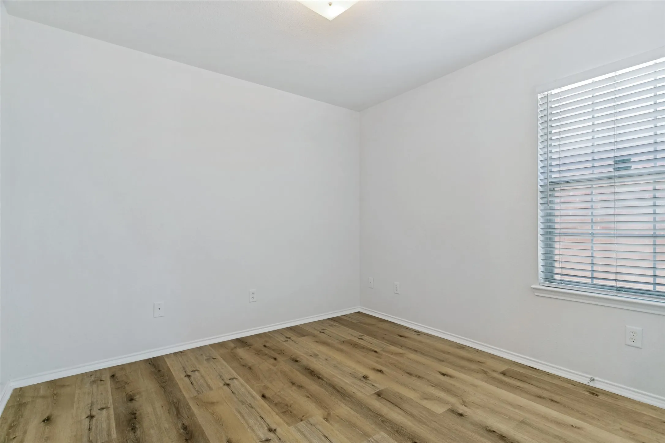 Hardwood-finish flooring, white walls, and a window with horizontal blinds