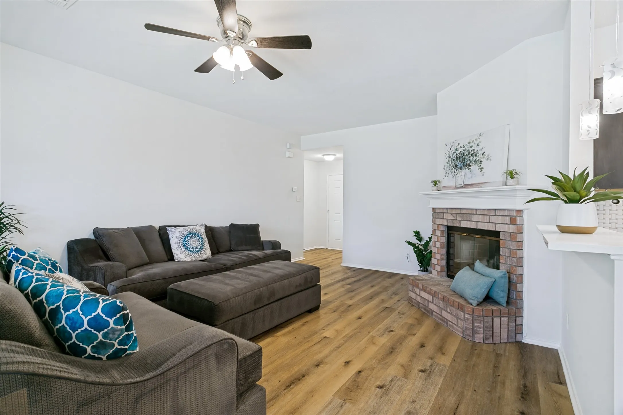 Wood-finish flooring throughout, brick-surround fireplace with hearth, built-in ceiling fan with light fixture, and pendant lighting