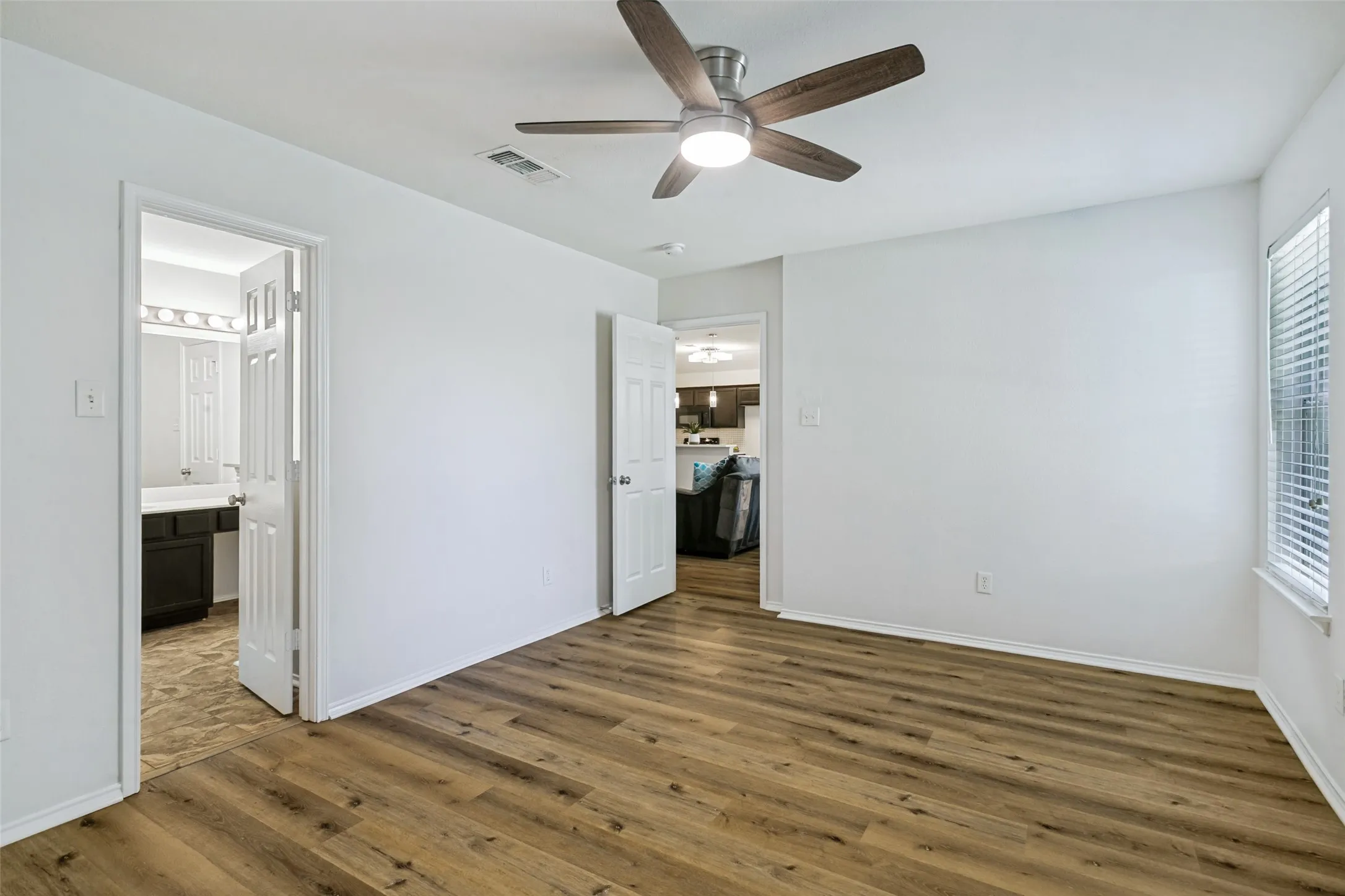 Wood-finish flooring, ceiling fan with integrated lighting, white walls, and white window blinds