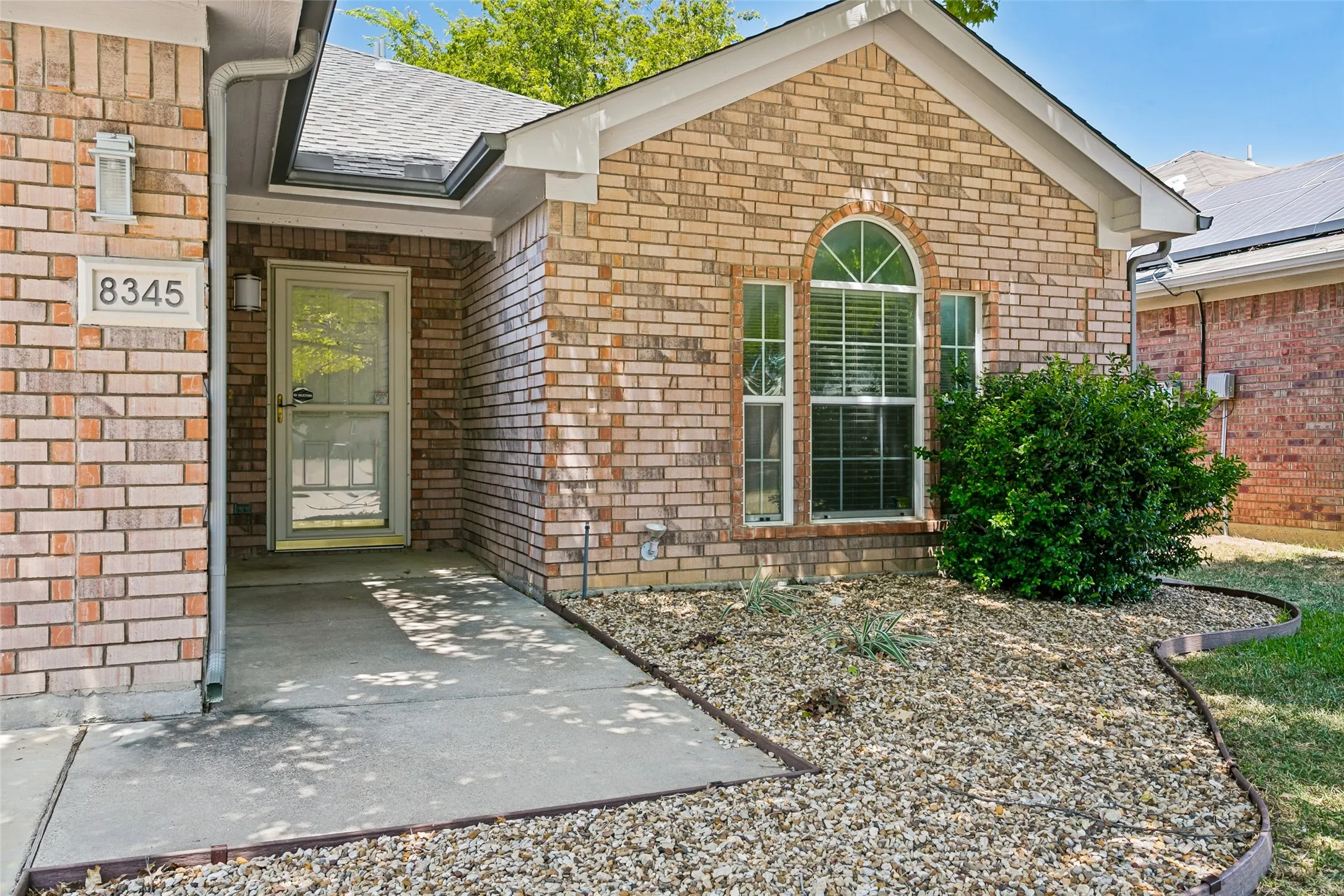 Brick exterior with a gabled roof, storm door and rock garden landscaping