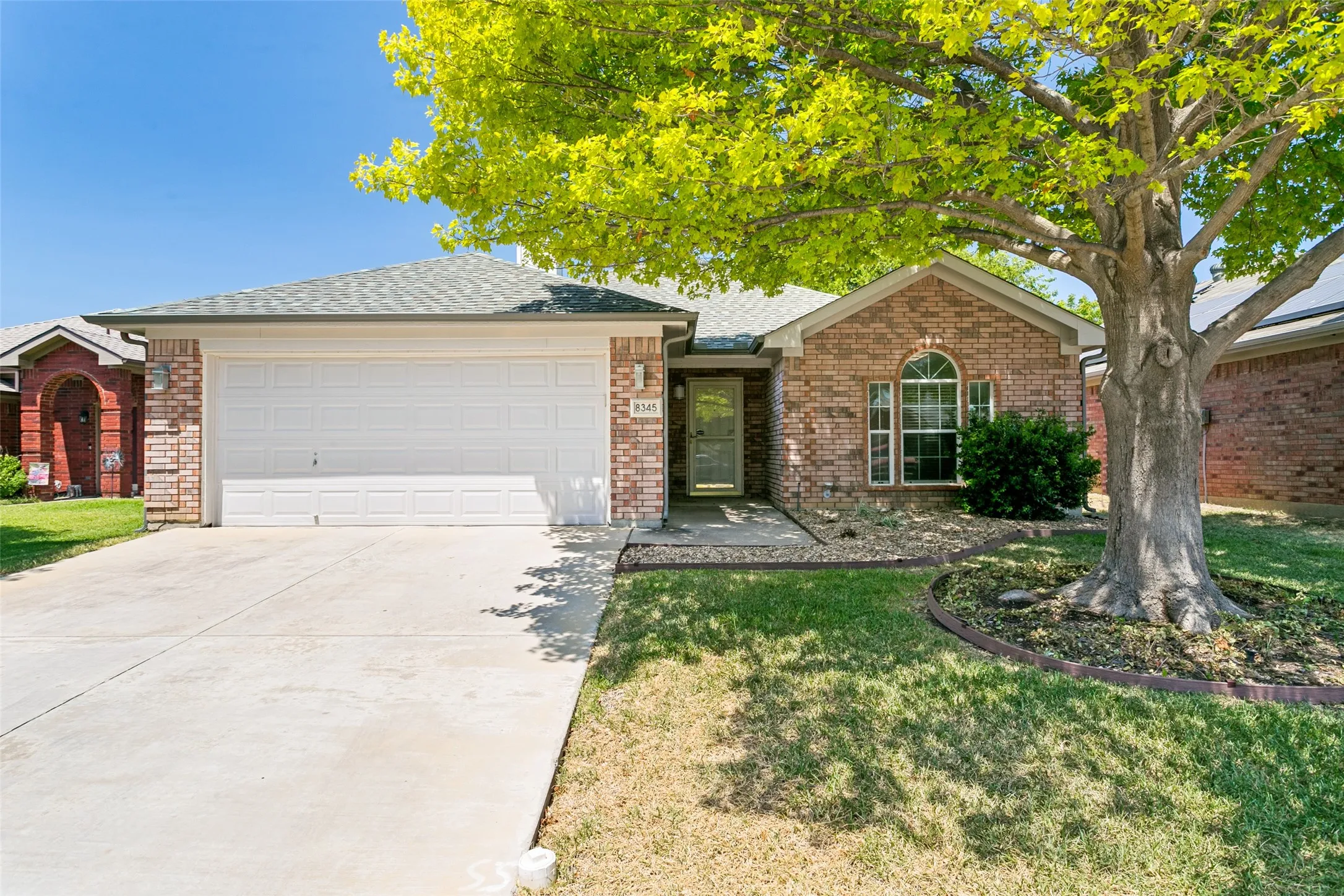 Brick exterior with an attached garage, arched window, front entry, and mature tree