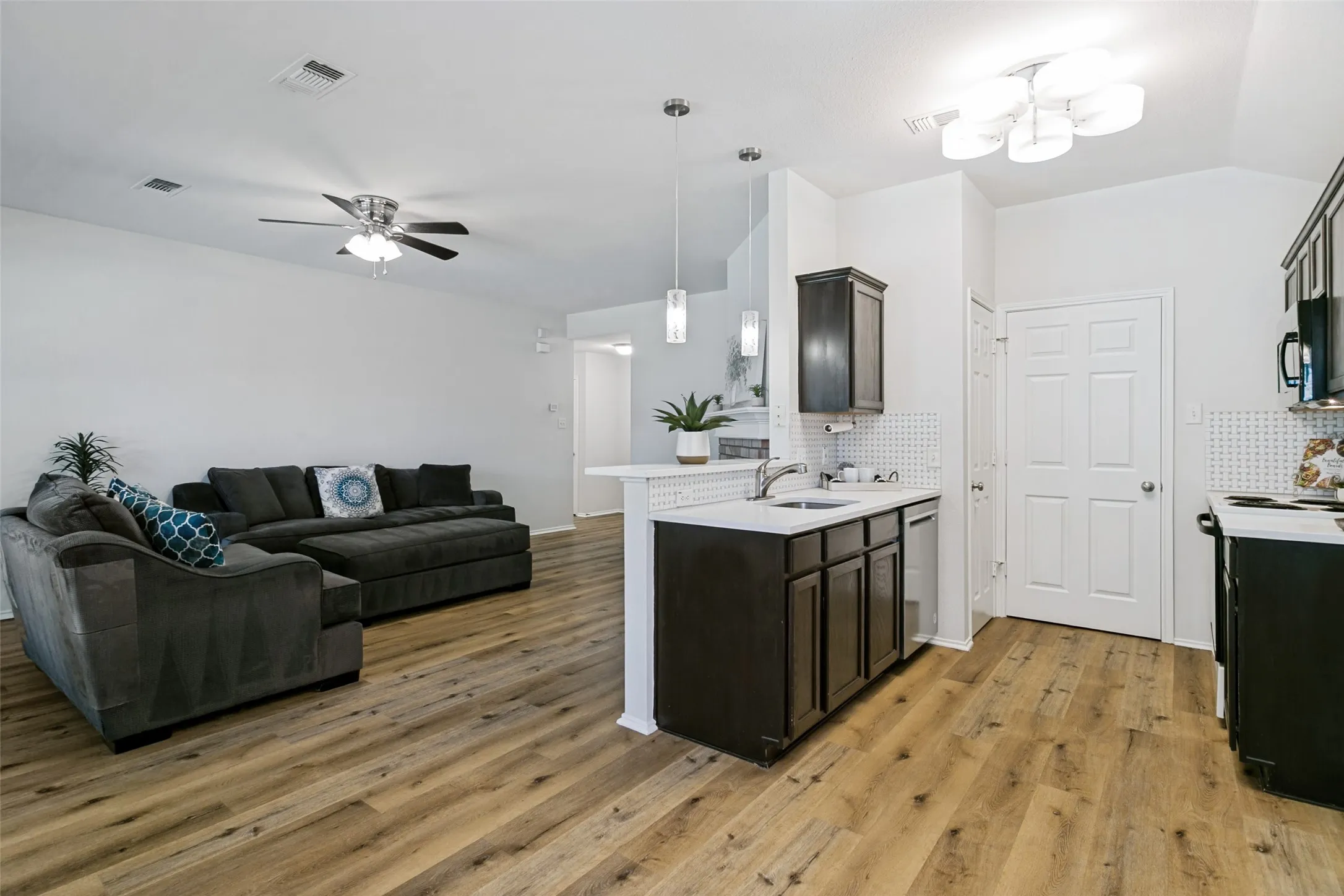 Wood-finish flooring throughout, bright white walls, modern ceiling fan, recessed lighting, and a kitchen island with pendant lighting