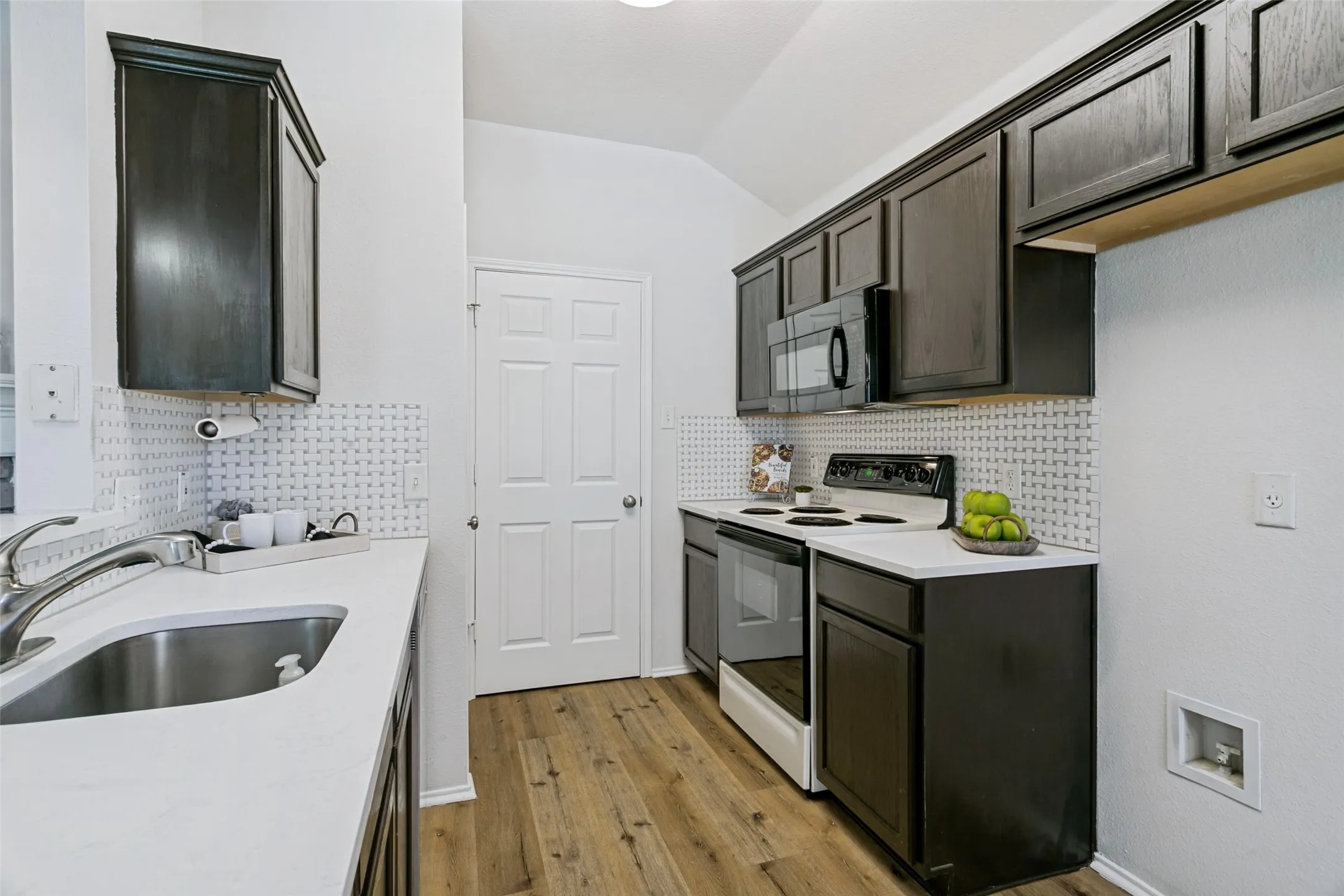 Kitchen featuring dark-finish cabinetry, stainless steel sink, white countertops, and wood-finish​​‌​​​​‌​​‌‌​‌‌​​​‌‌​‌​‌​‌​​​‌​​ flooring