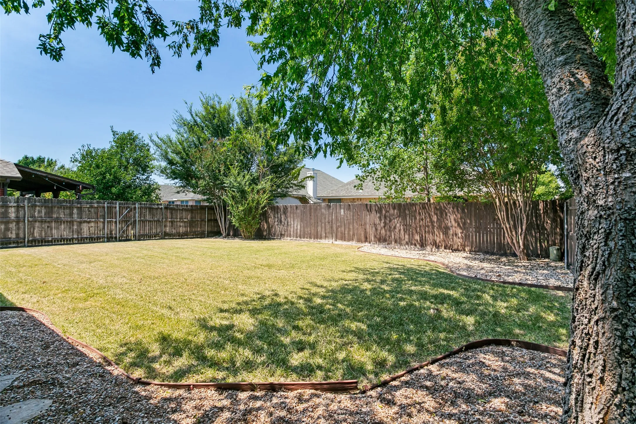 Expansive backyard featuring a manicured lawn, established perimeter fencing, and mature trees providing natural shade