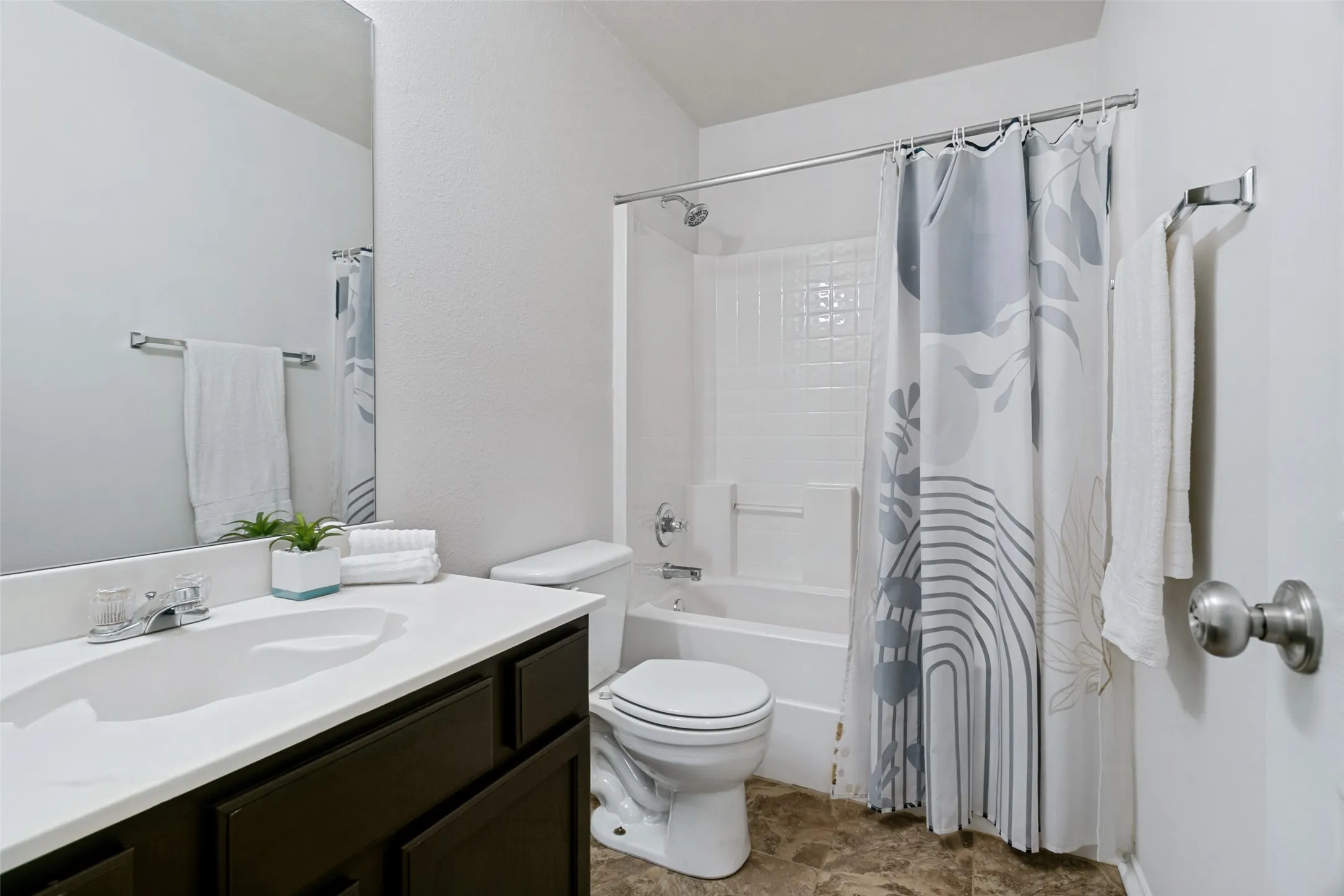 White countertop vanity with dark wood-finish cabinetry, a large wall-mounted mirror, and a full bathtub with a shower