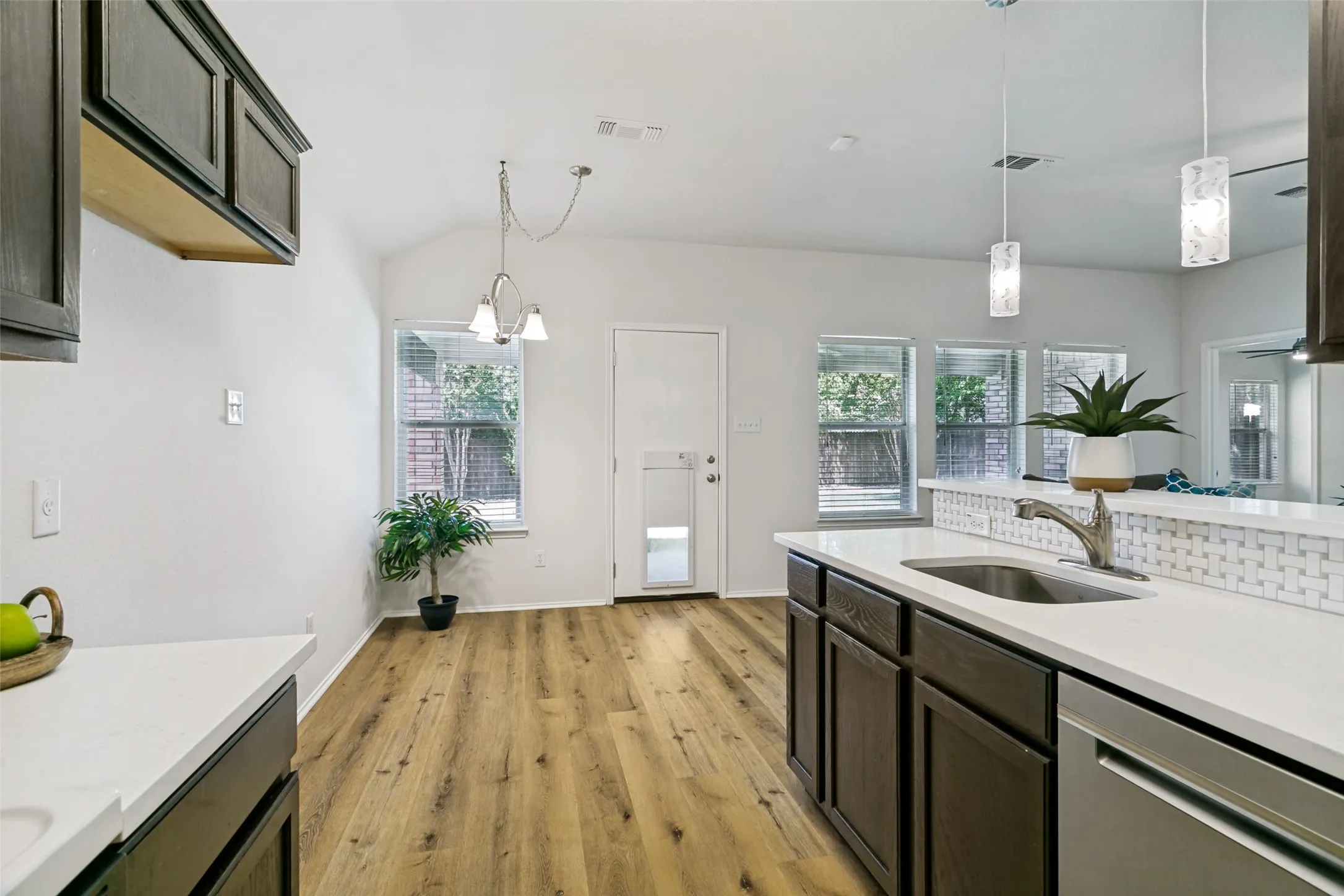 Vaulted ceiling, wood-finish flooring, white countertops, built-in dark wood cabinetry, and stainless steel dishwasher