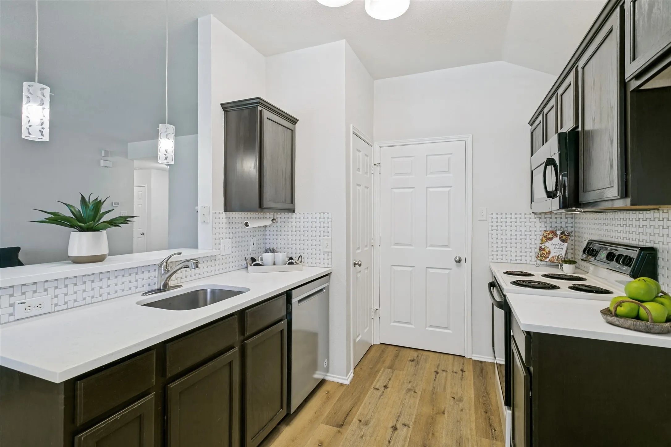 Kitchen with white countertops, wood-finish flooring, dark wood cabinetry, stainless steel sink, and white patterned tile backsplash