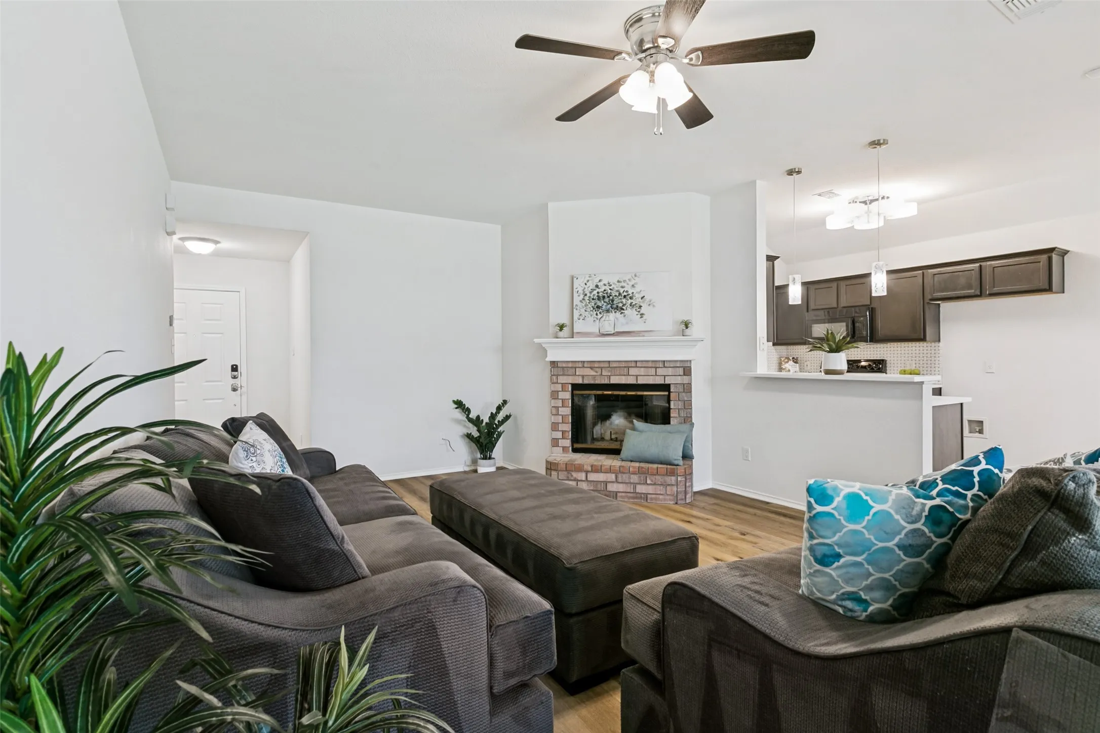 Living area featuring a brick fireplace with a white mantel, wood-finish flooring, and a ceiling fan
