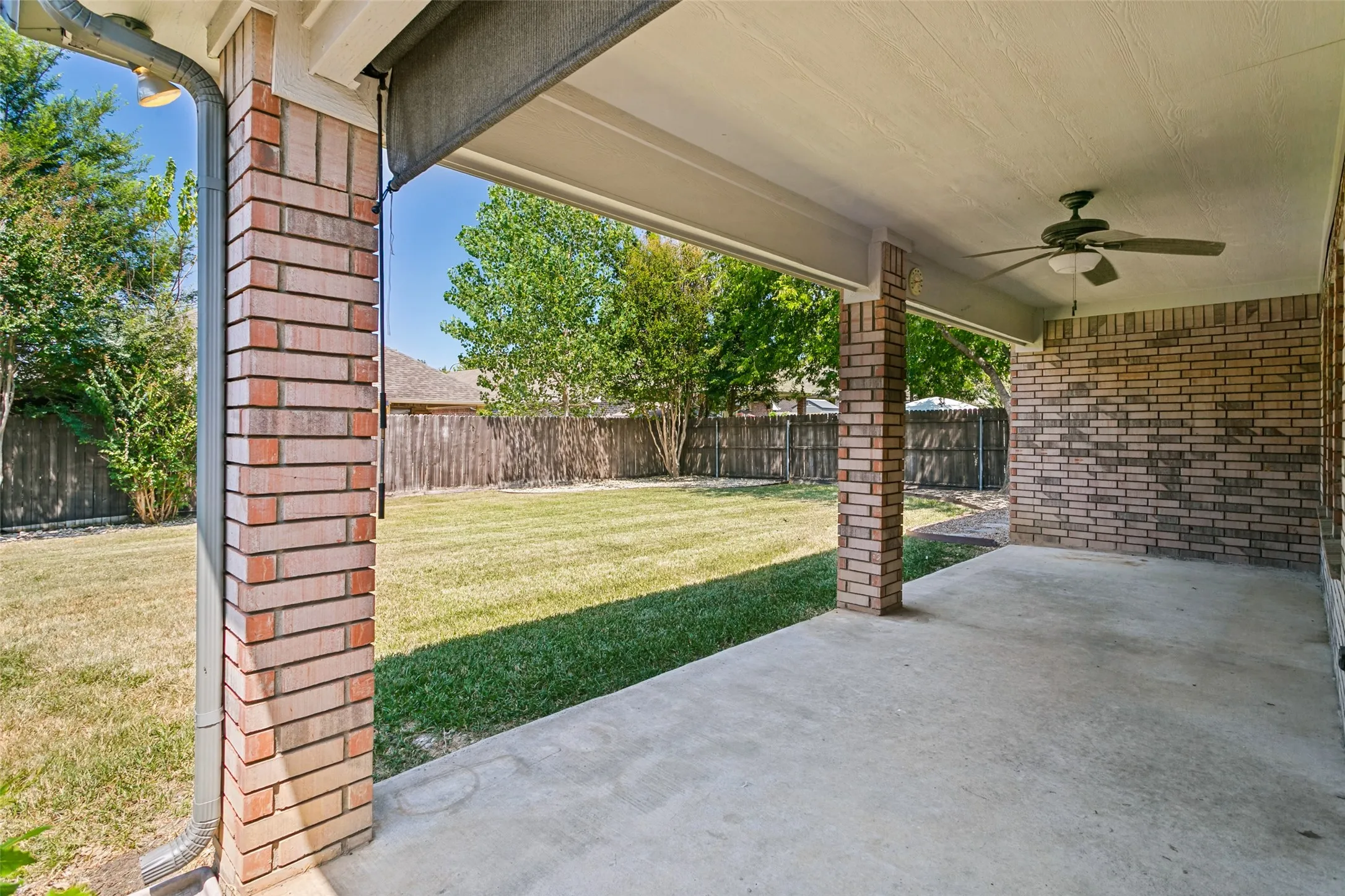 Covered patio featuring brick pillars, an outdoor ceiling fan, and a concrete floor