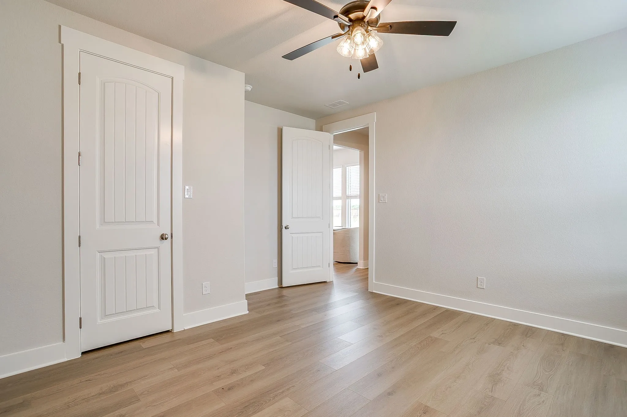 Wood-finish flooring, ceiling fan with integrated lighting, paneled interior doors, and white trim throughout