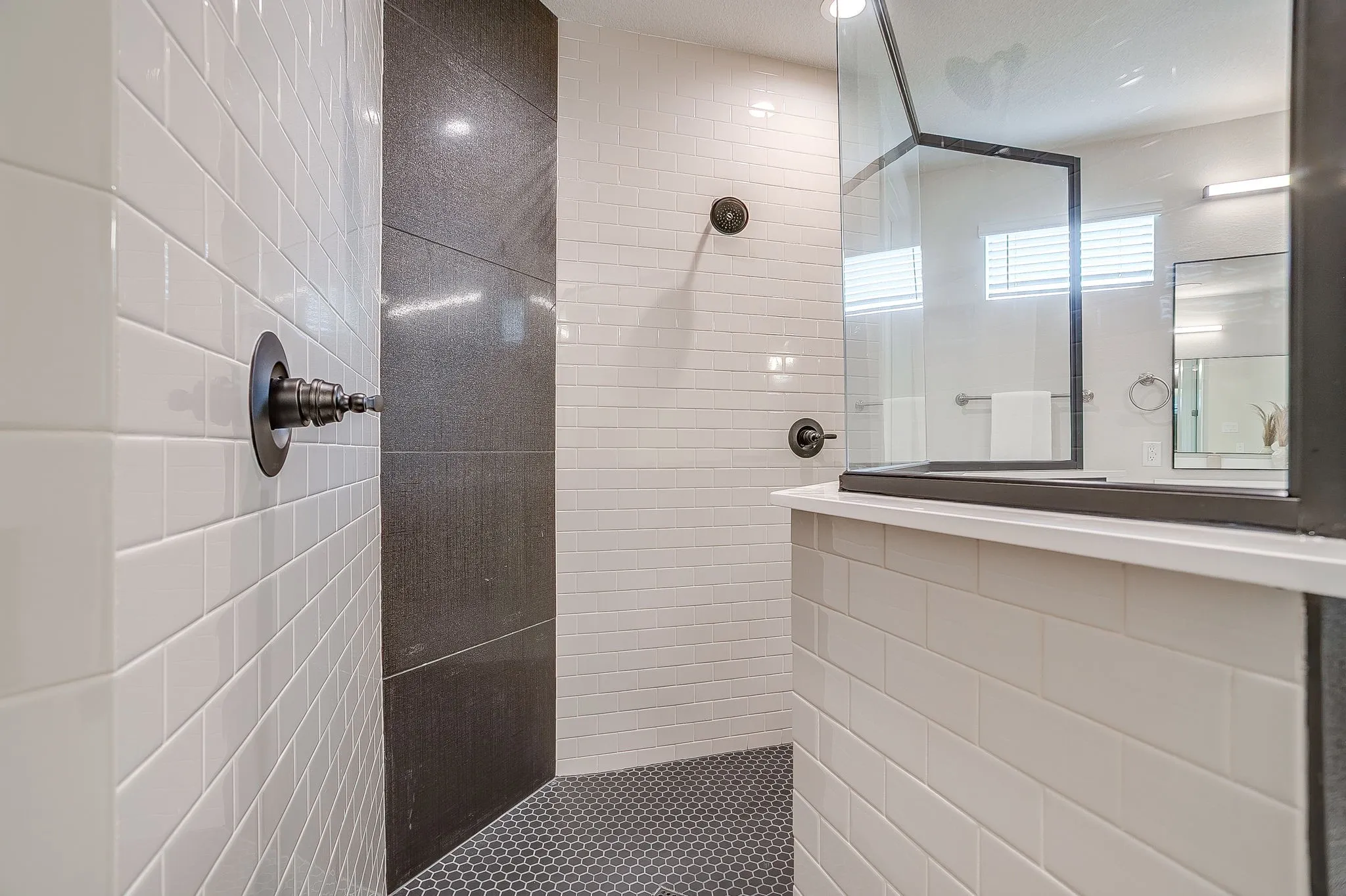 Walk-in shower with white subway tile walls, dark accent tile, dark hexagonal floor tiling, and a glass enclosure with dark framing