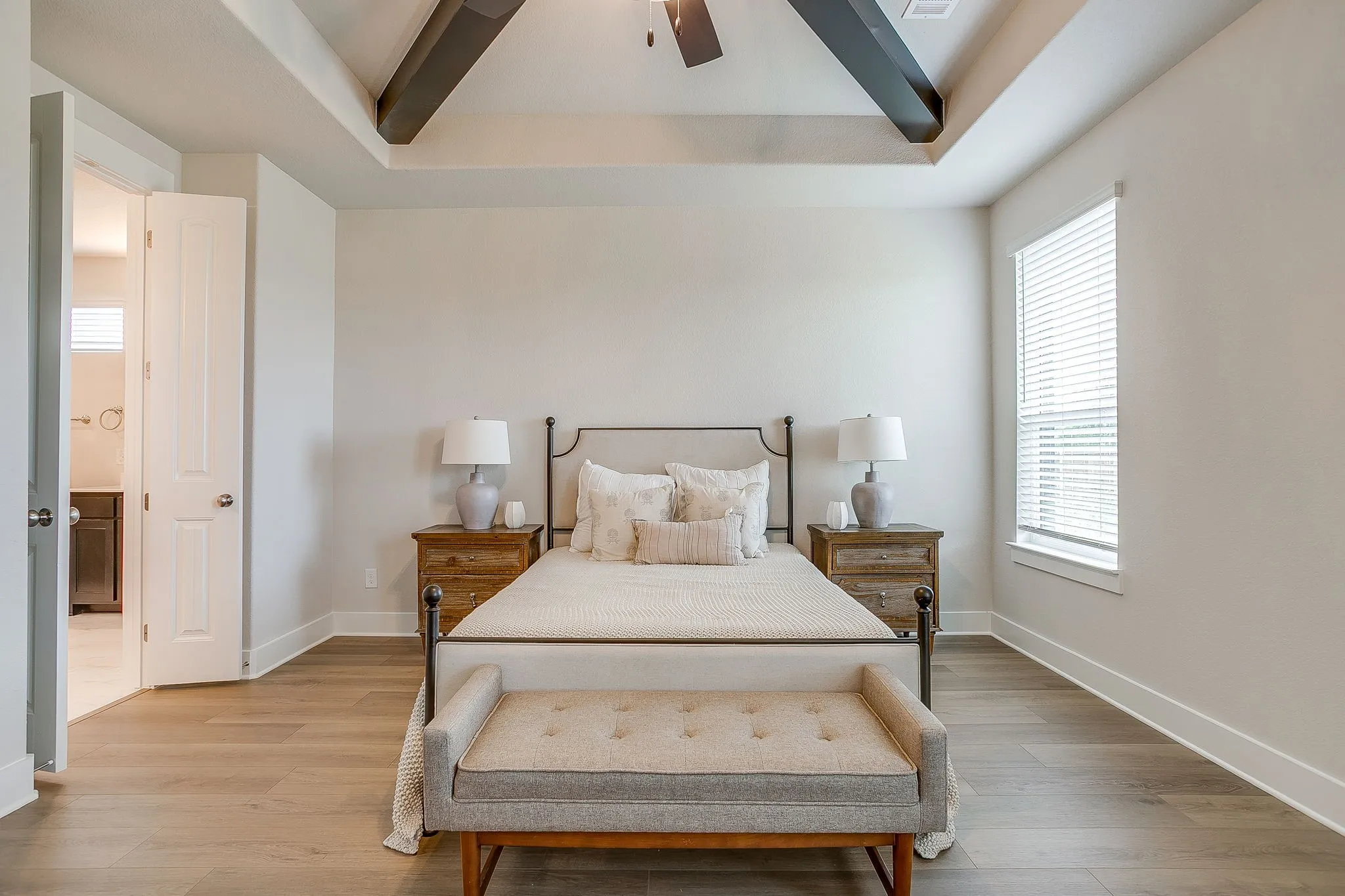 Tray ceiling with dark wood beams, light wood-finish flooring, white walls, and a window with blinds