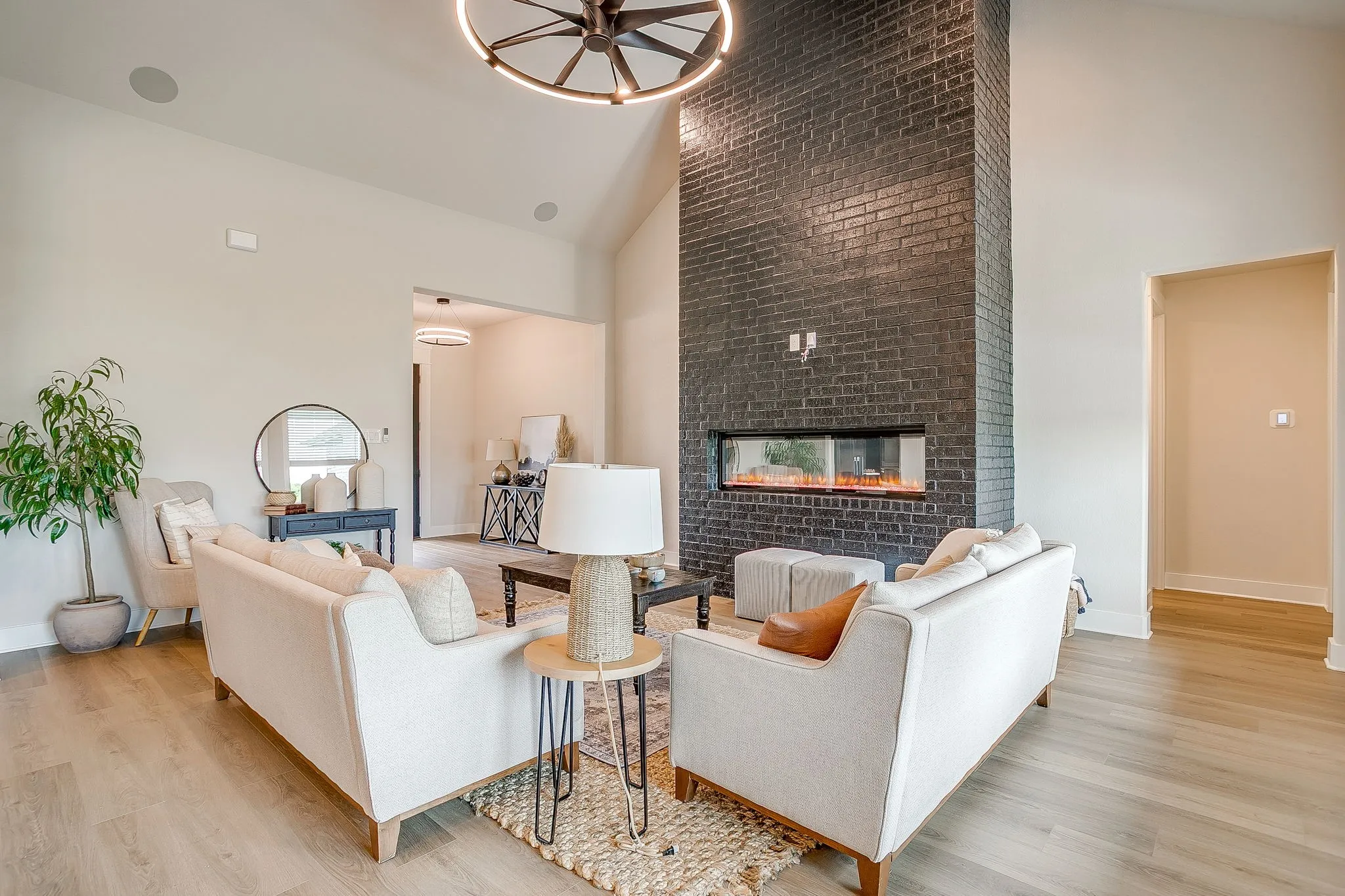 Vaulted ceiling, wood-finish flooring, dark brick fireplace, linear electric fireplace, and a contemporary ceiling fixture