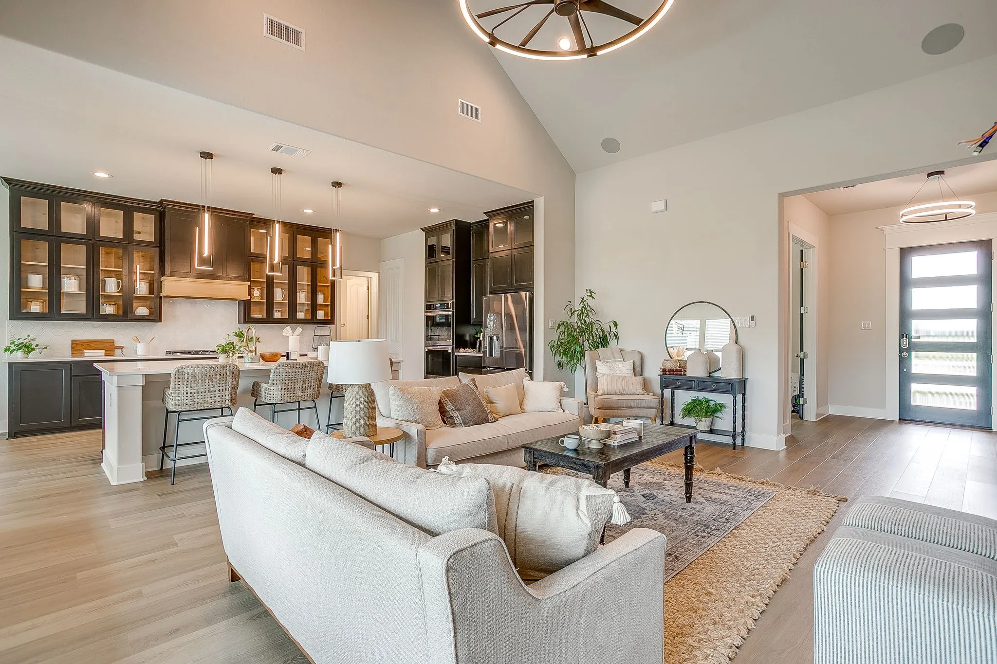 Vaulted ceiling, wood-finish flooring, recessed lighting, and a kitchen featuring dark cabinetry with glass-front uppers and pendant lighting
