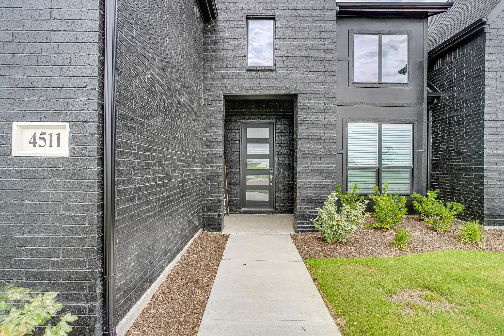 Contemporary brick exterior with a prominent entrance, modern front door featuring frosted glass panels, and well-maintained landscaping