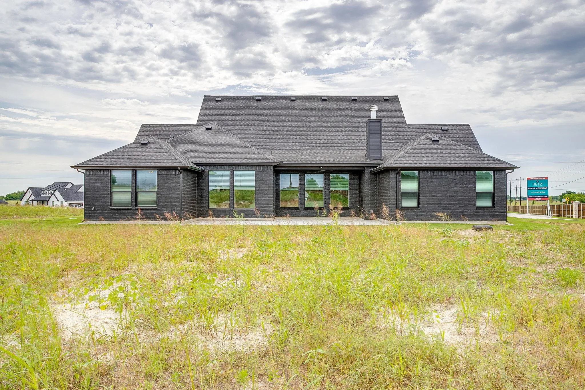 Contemporary exterior featuring dark brick, a gray shingle roof, a rear patio, and multiple large windows