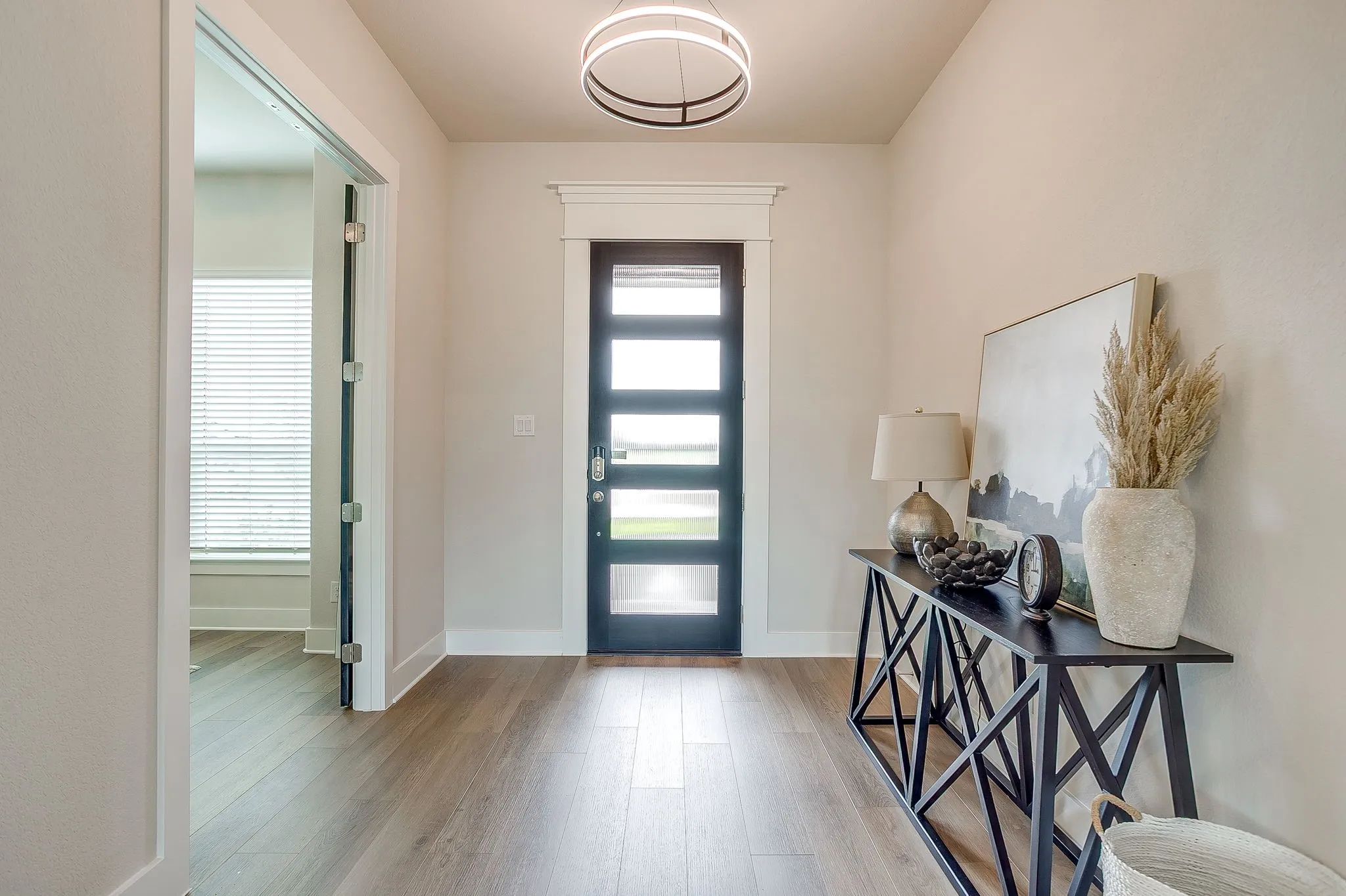 Entryway featuring wood-finish flooring, a contemporary ceiling light fixture, a dark-framed glass paneled door, and a glass-paneled interior door