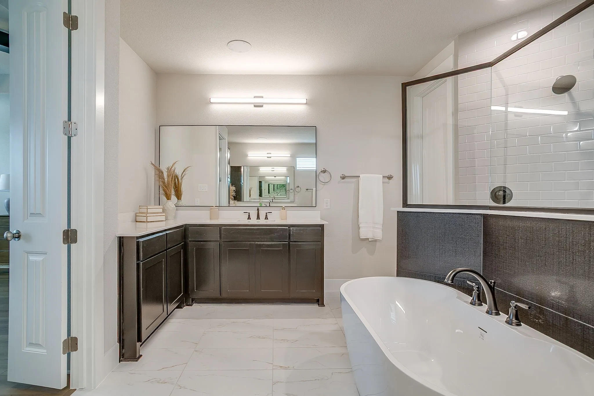 Dual vanity with dark wood cabinetry and light-toned countertops, freestanding soaking tub, and a glass-enclosed shower with subway tile