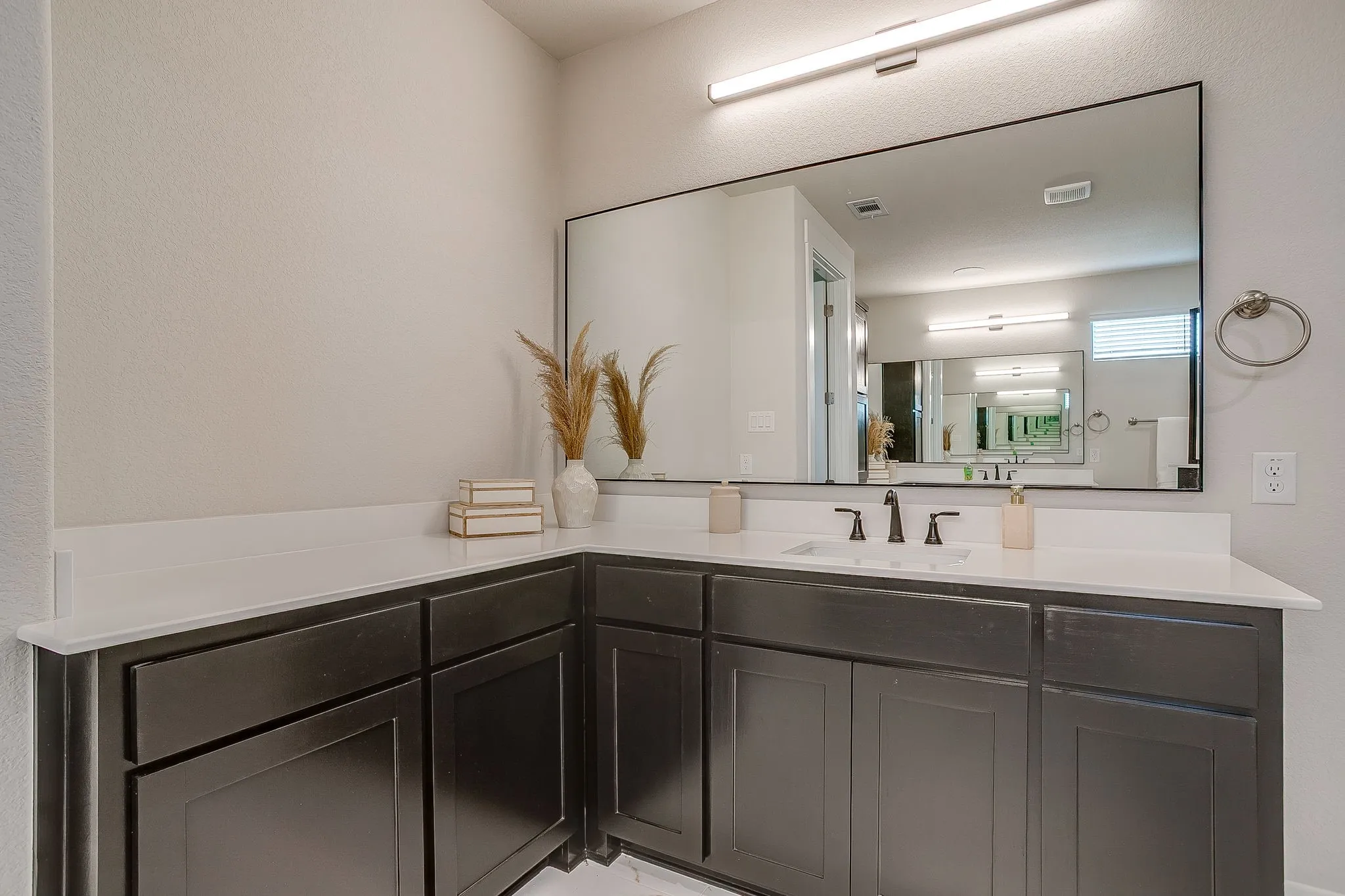 L-shaped vanity with dark wood-finish cabinetry, white countertop, rectangular undermount sink, and matte black faucet