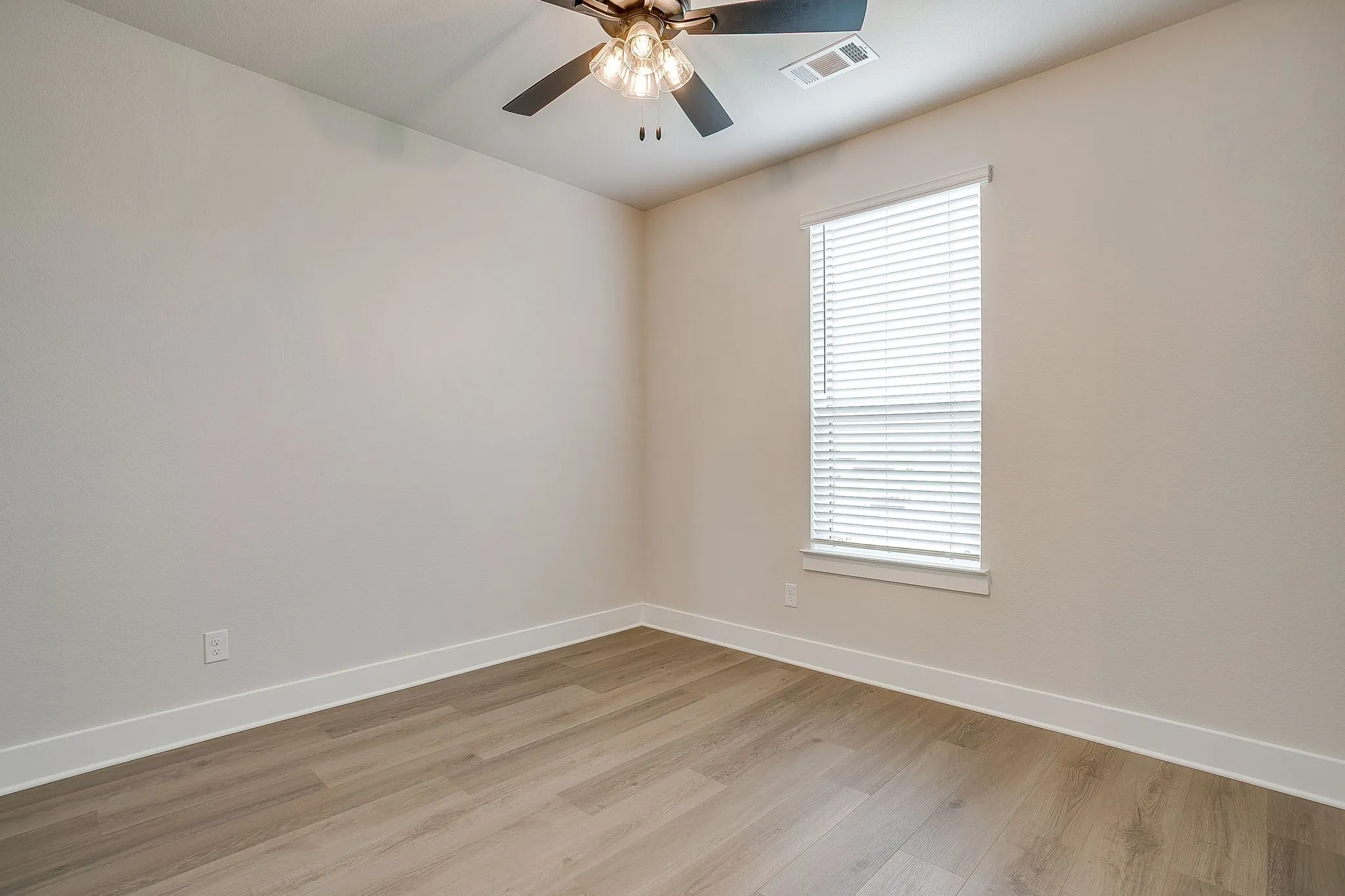 Wood-finish flooring, neutral wall tones, window with horizontal blinds, and a ceiling fan with integrated lighting