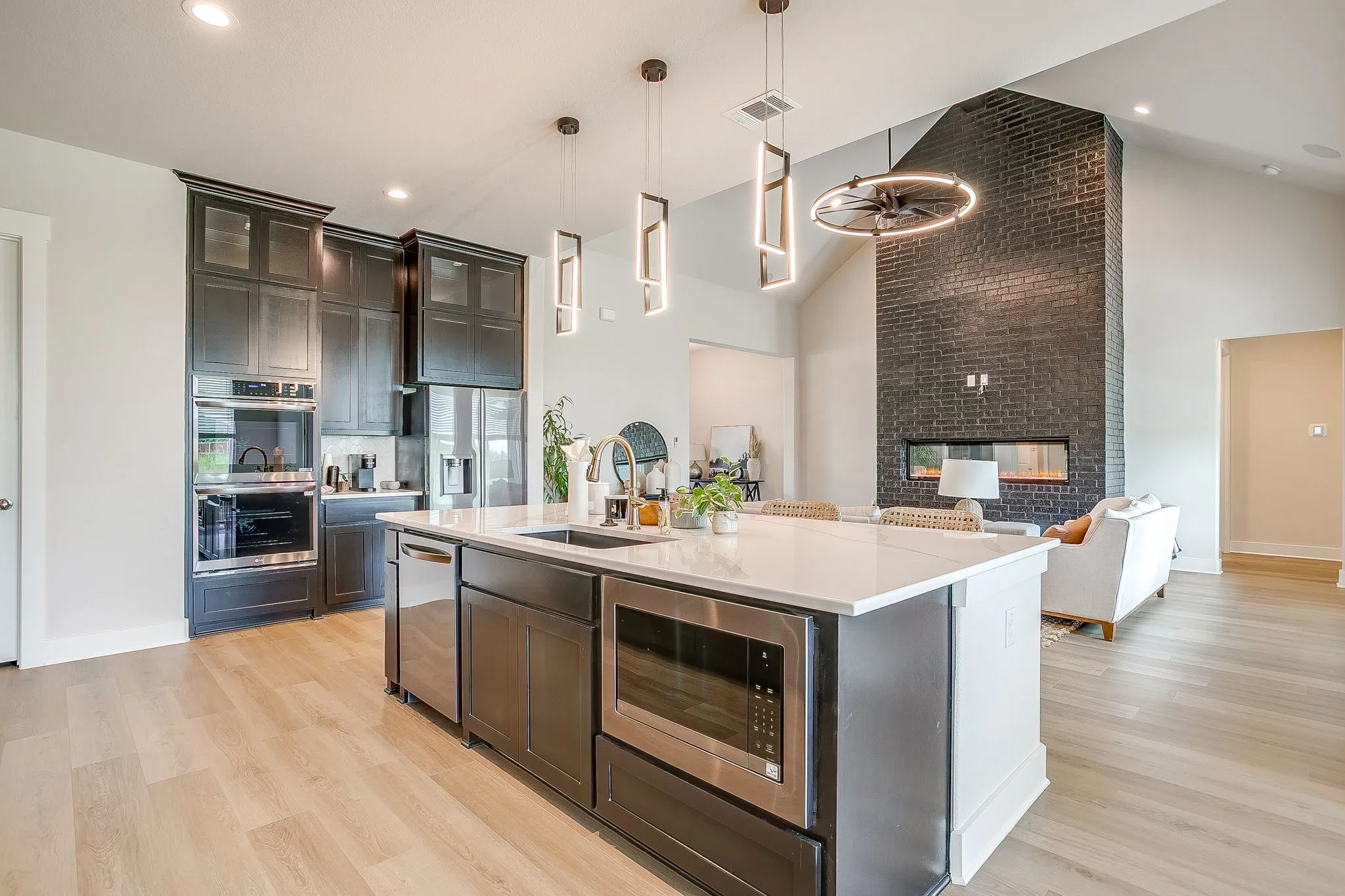 Spacious kitchen featuring an expansive island with an undermount sink and stainless steel appliances, dark wood-finish cabinetry, and wood-finish flooring
