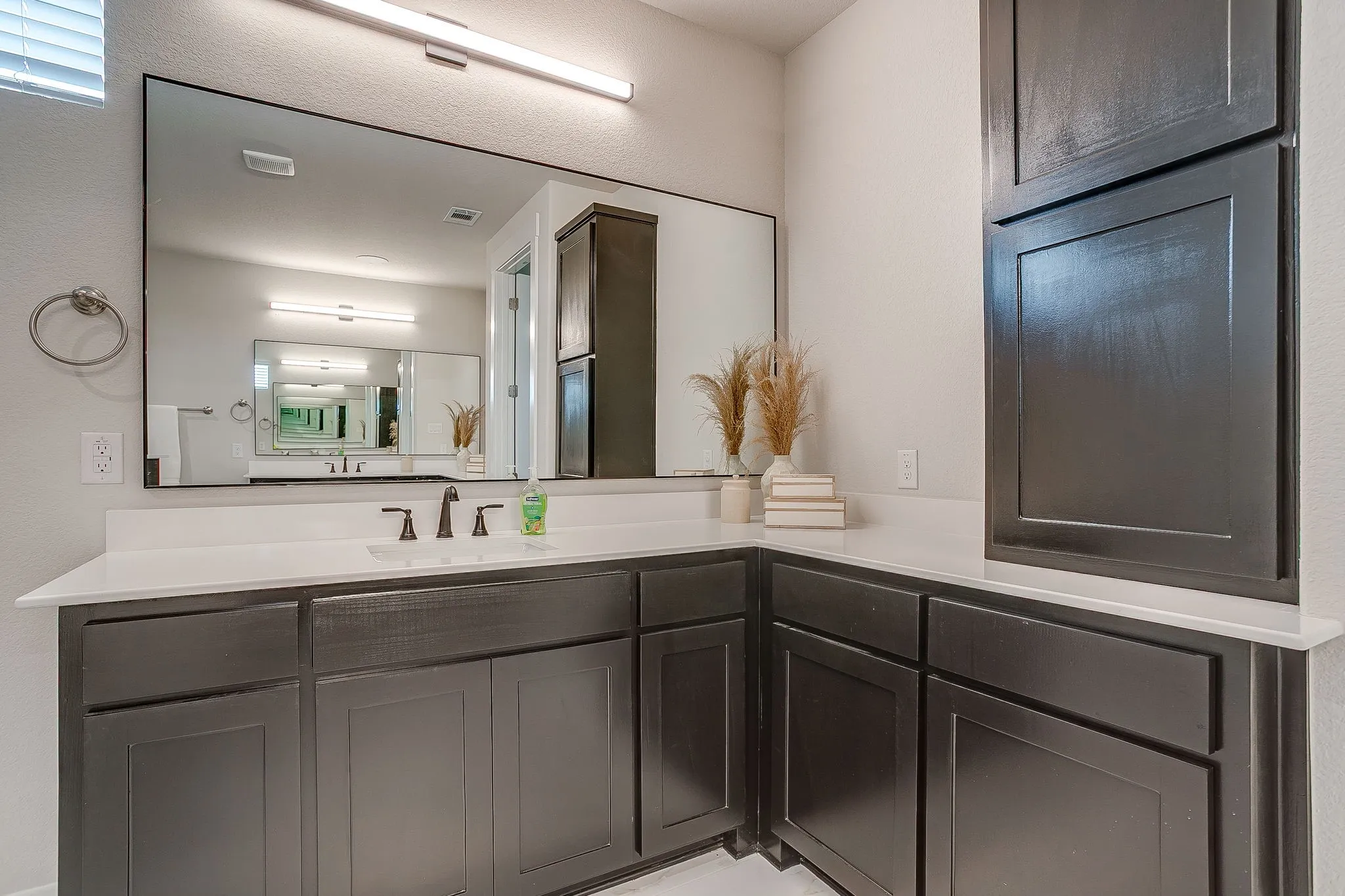 Spacious vanity with dark wood-finish cabinetry, white countertop, integrated sink, and an expansive mirror