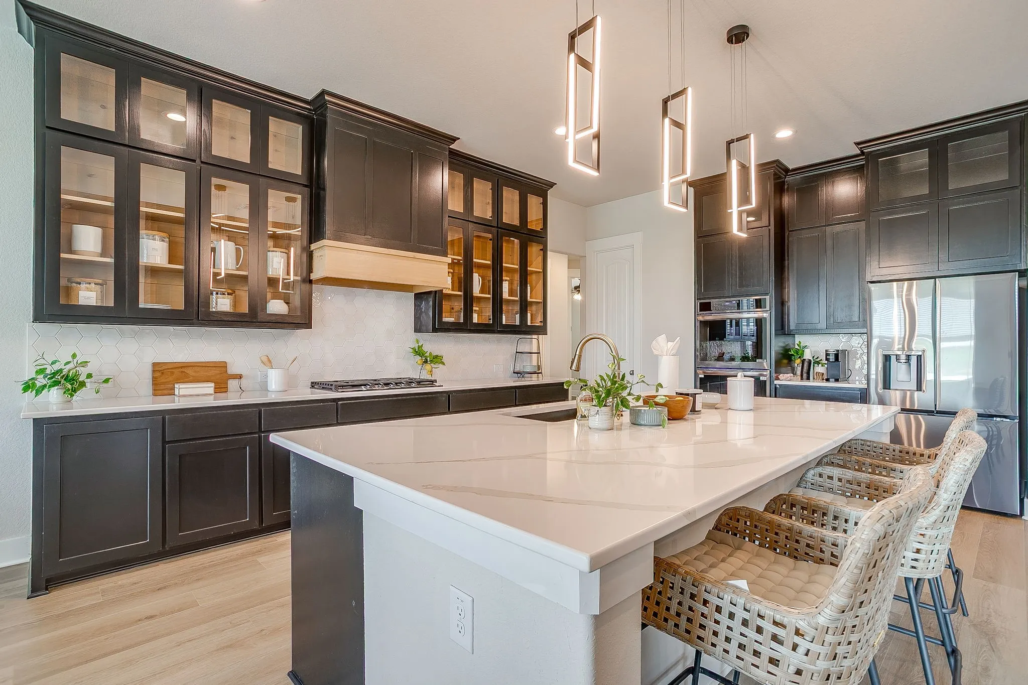 Central kitchen island with a stone countertop, dark cabinetry with glass-front uppers, stainless steel appliances, a tile backsplash, and wood-finish flooring
