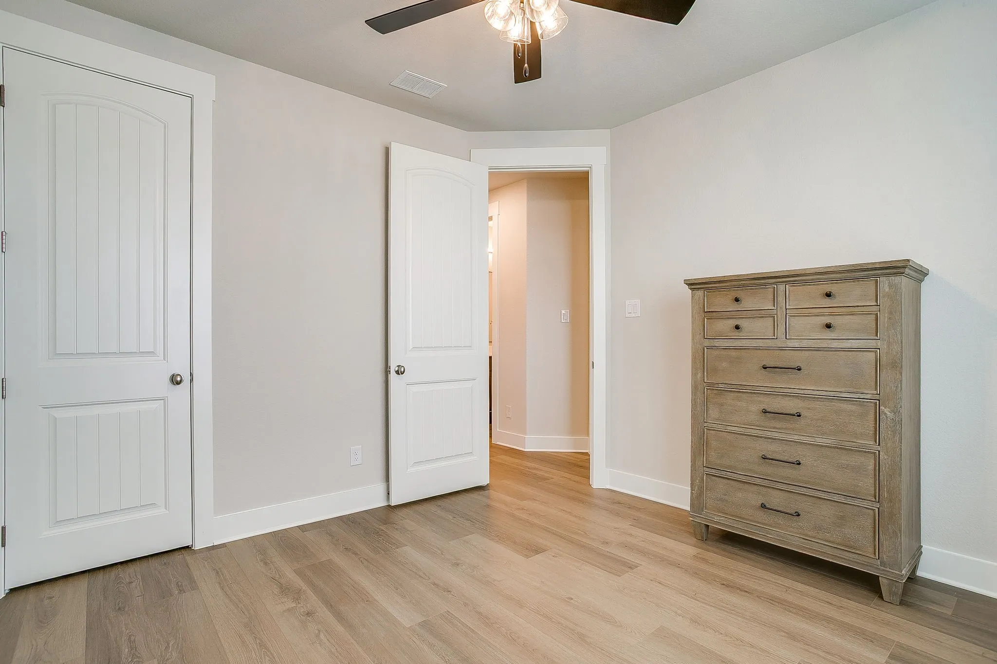 Wood-finish flooring throughout, white trim, and a ceiling fan with integrated lighting