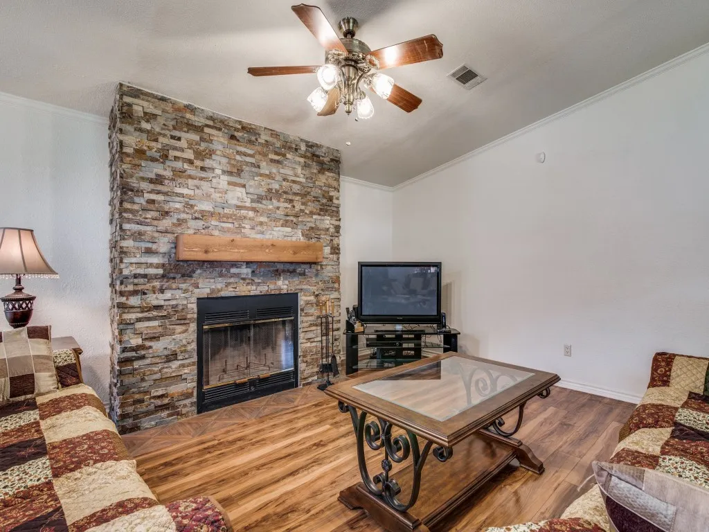 Stone-clad fireplace with a wood mantel, wood-finish flooring, and a ceiling fan with integrated lighting