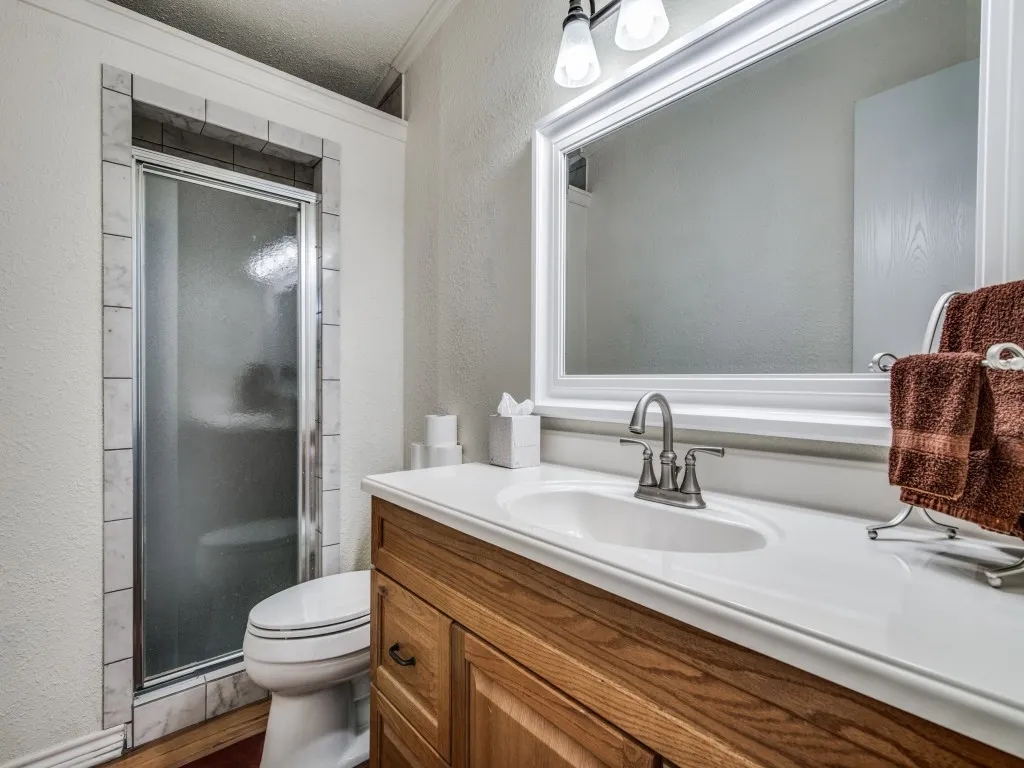 Wood-finish vanity with an integrated sink and brushed nickel faucet, large framed mirror, and a tiled shower with a sliding glass door