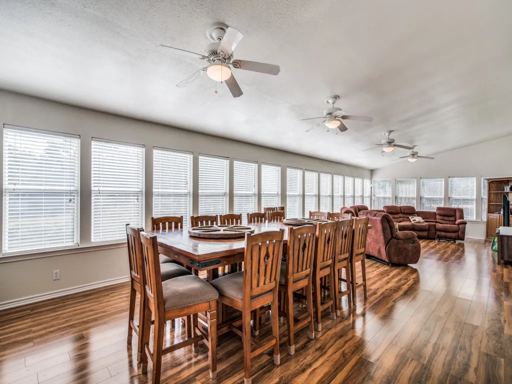 Expansive room featuring multiple windows with blinds, wood-finish flooring, and multiple ceiling fans
