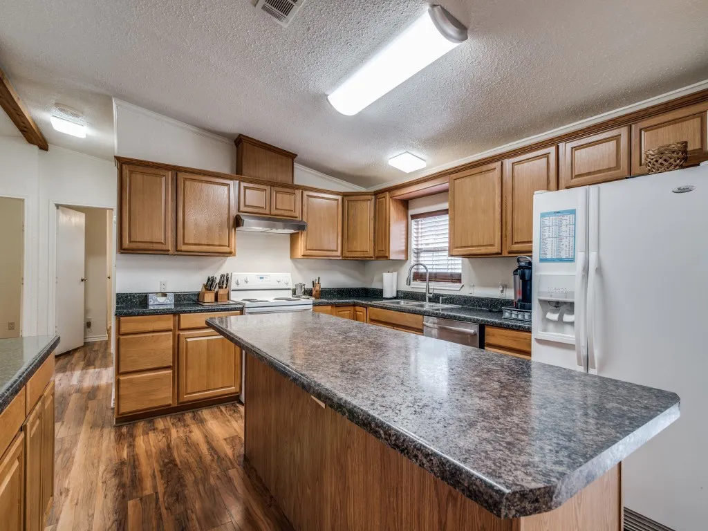 Kitchen featuring a central island, wood-finish flooring, wood cabinetry, dark countertops, and a white refrigerator
