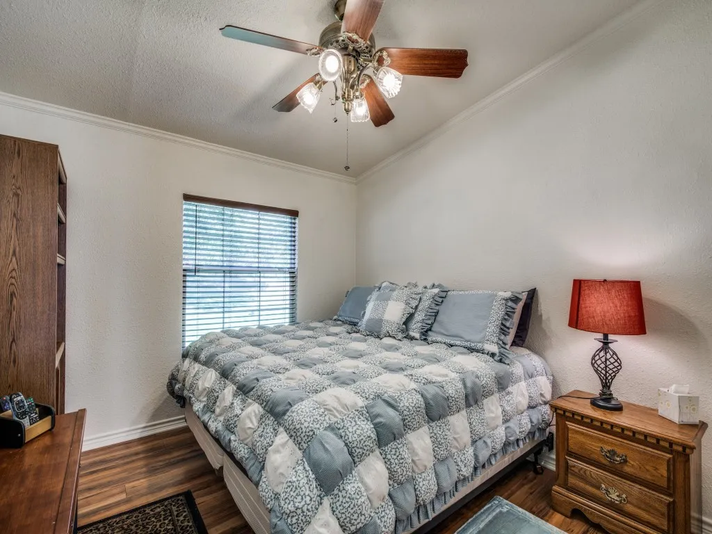 Wood-finish flooring, white painted walls, vaulted ceiling, crown molding, and a ceiling fan with integrated lighting