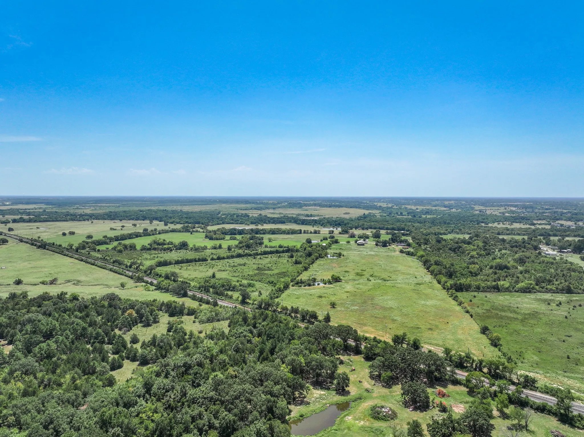 Expansive property featuring varied terrain, including open fields, wooded areas, and a visible pond