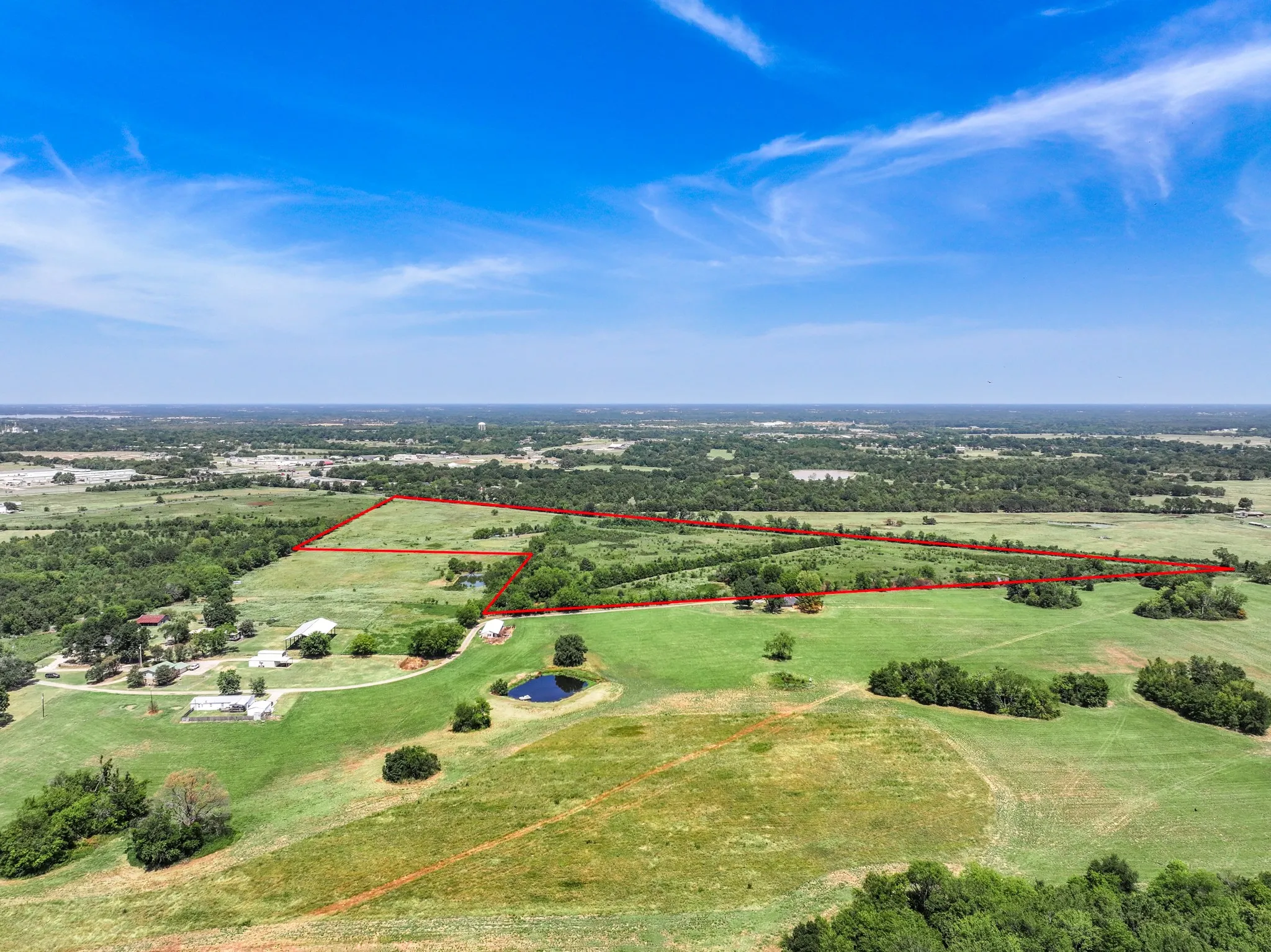 Expansive land parcel featuring a natural pond, lush green fields, and scattered mature trees