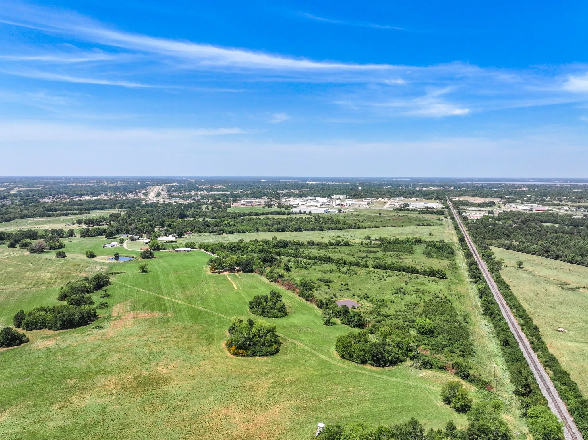 Expansive green spaces with scattered trees, a visible pond, and distant structures under a clear sky