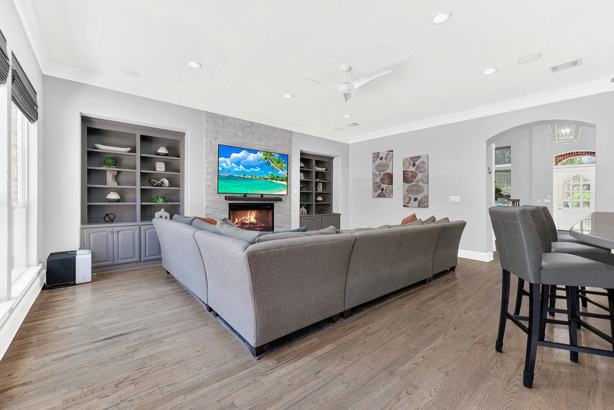 Custom built-in shelving flanks a cozy stacked-stone fireplace in this spacious room that connects smoothly toward the main foyer. Unwind after a long day with movie nights by a warm fire while enjoying a seamless, welcoming home layout.