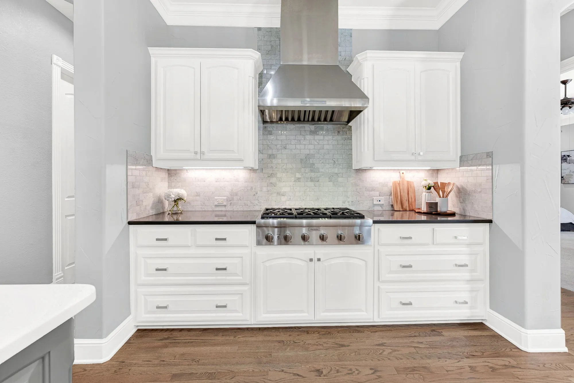 A professional Thermador gas rangetop features a stainless hood and handsome stone tile backsplash. Prepare your favorite gourmet recipes with ease while feeling like a master chef in your own home.