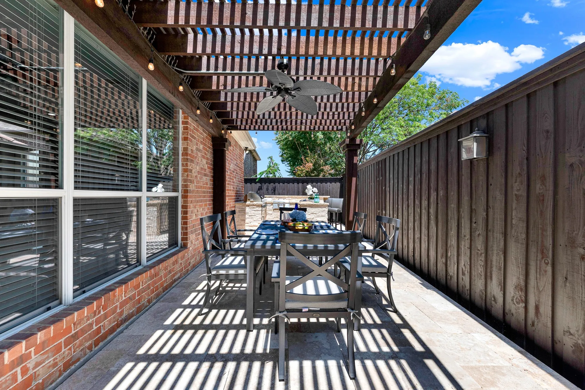 A rustic wooden pergola with string lights, ceiling fan, and four outdoor speakers shelters this outdoor dining space. Enjoy alfresco dinners and evening drinks in a warm, atmosphere-rich setting.