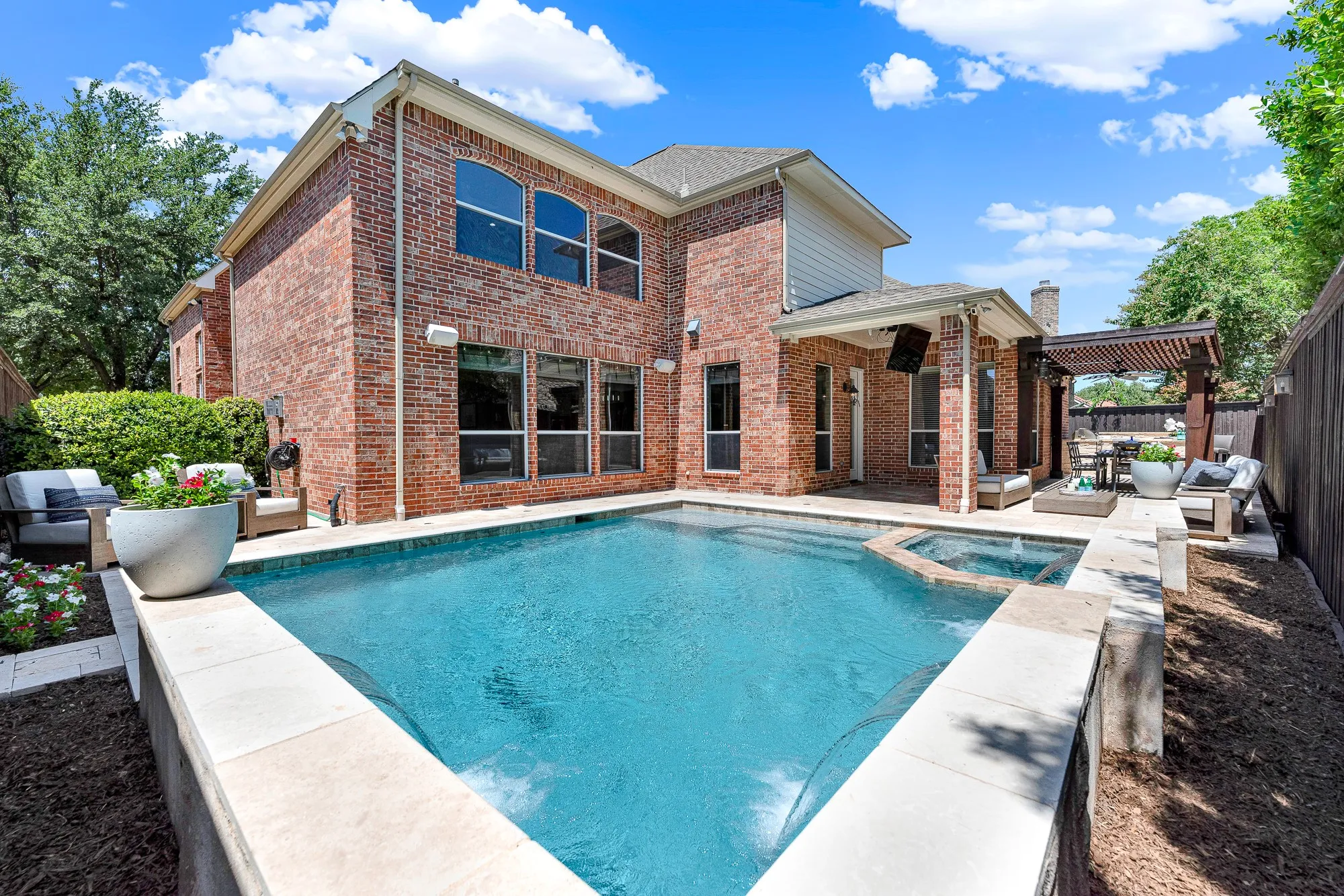 This custom pool setup highlights a separate hot tub, travertine stone decking, and a built-in auto-fill system that automatically maintains proper water level. Host unforgettable weekend gatherings, evening swims, and outdoor dinners in your own private backyard oasis.