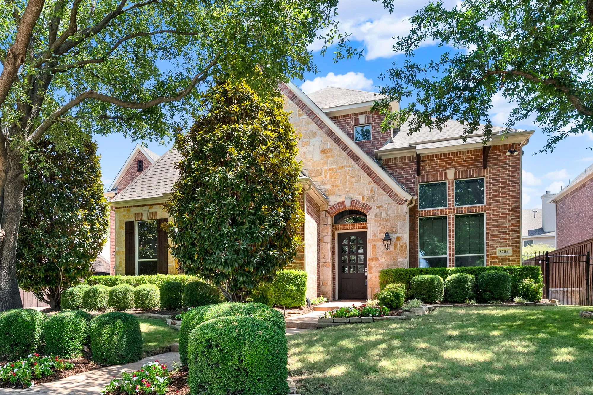  A stone and brick facade is surrounded by manicured hedge landscaping, mature shade trees, and a flagstone walkway. Arrive home to exceptional curb appeal that welcomes family and guests with warmth and timeless elegance.