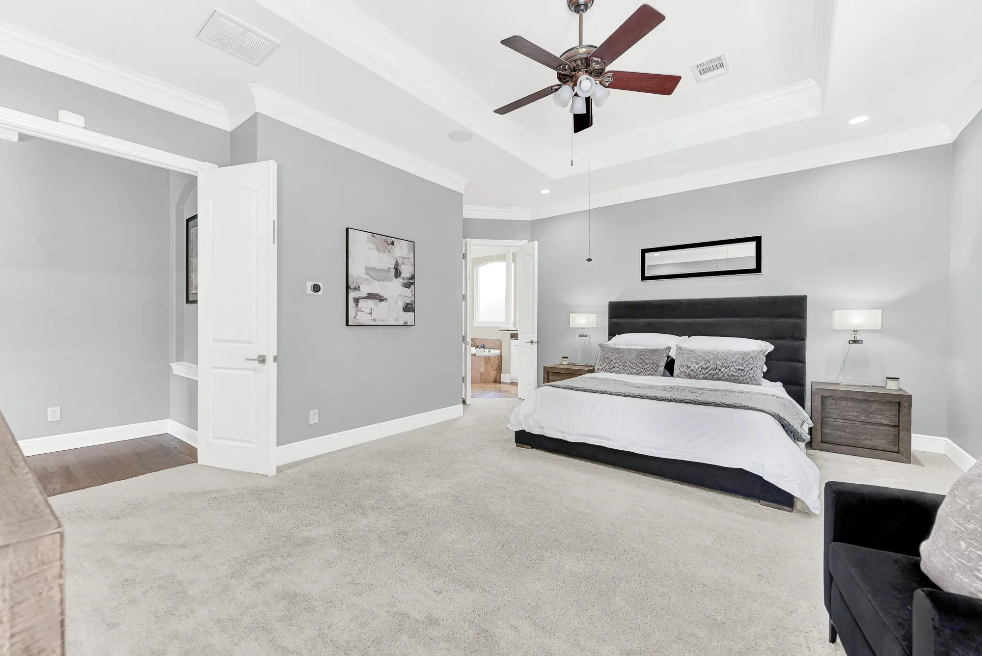 Tray ceiling detail, plush carpeting, and two built-in Sonance speakers connected to the whole-home audio system anchor this spacious main-level suite. Set your favorite relaxing playlist and enjoy a seamless transition into the primary bath each morning