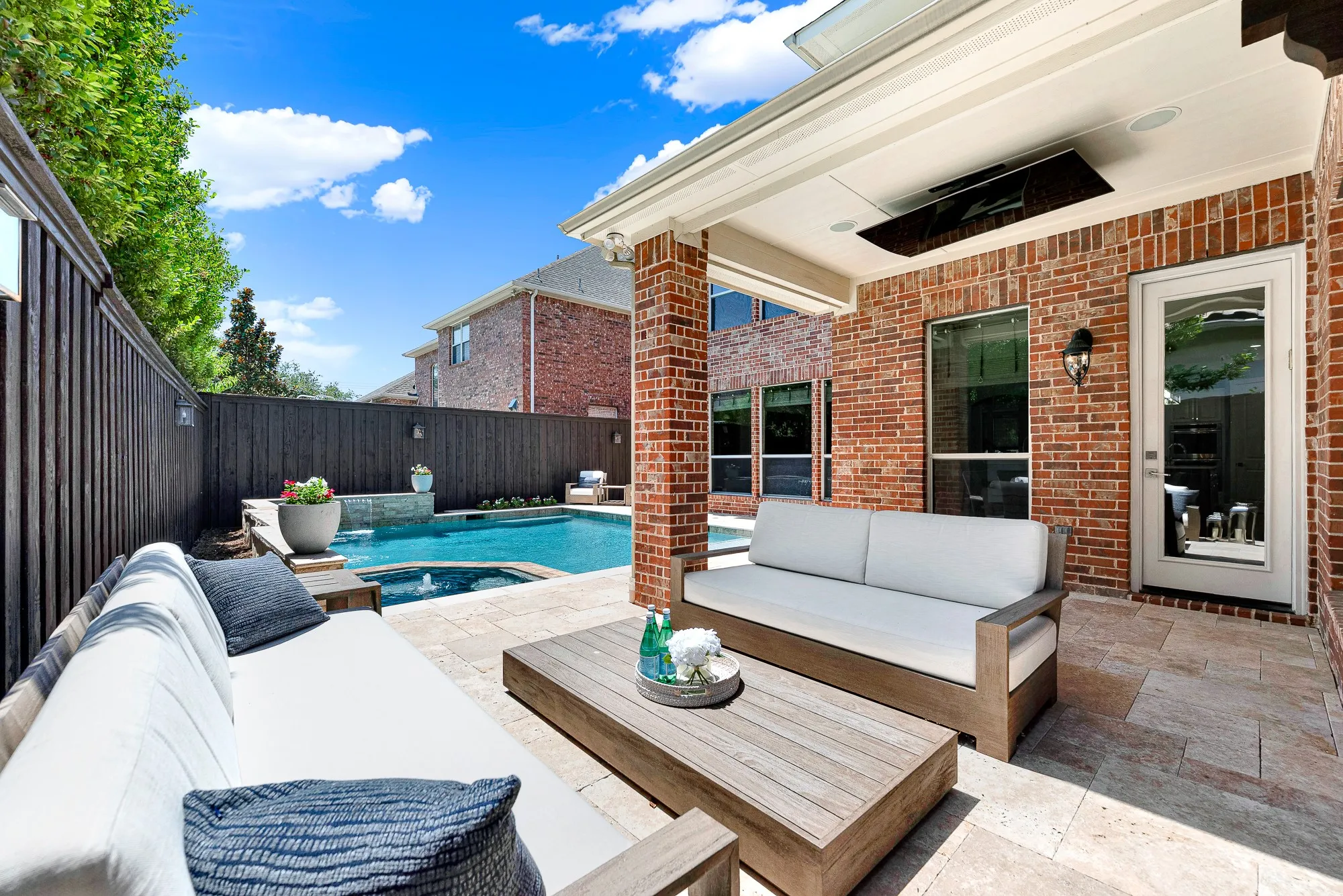 The shaded oasis reveals a cozy living area with comfortable seating and a rustic wood coffee table, transitioning seamlessly to the pristine pool and private, enclosed yard. This inviting space is designed for entertaining, allowing you to host unforgettable summer gatherings where your friends can easily socialize while enjoying the view.