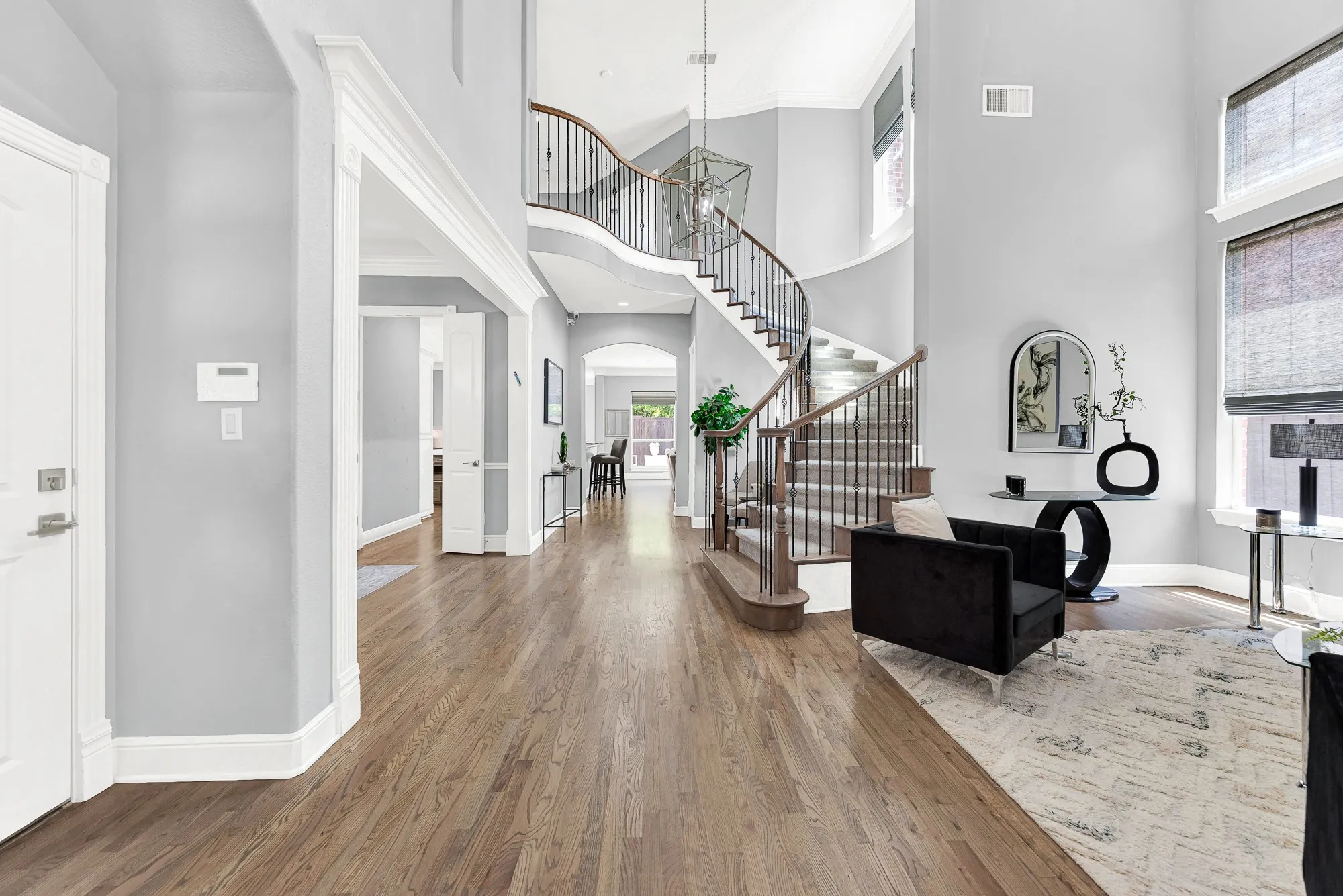 A sweeping curved staircase with wrought-iron balusters and rich hardwood floors creates a grand impression upon entry. Greet incoming friends and family warmly in an elegant foyer designed for bright, welcoming arrivals.