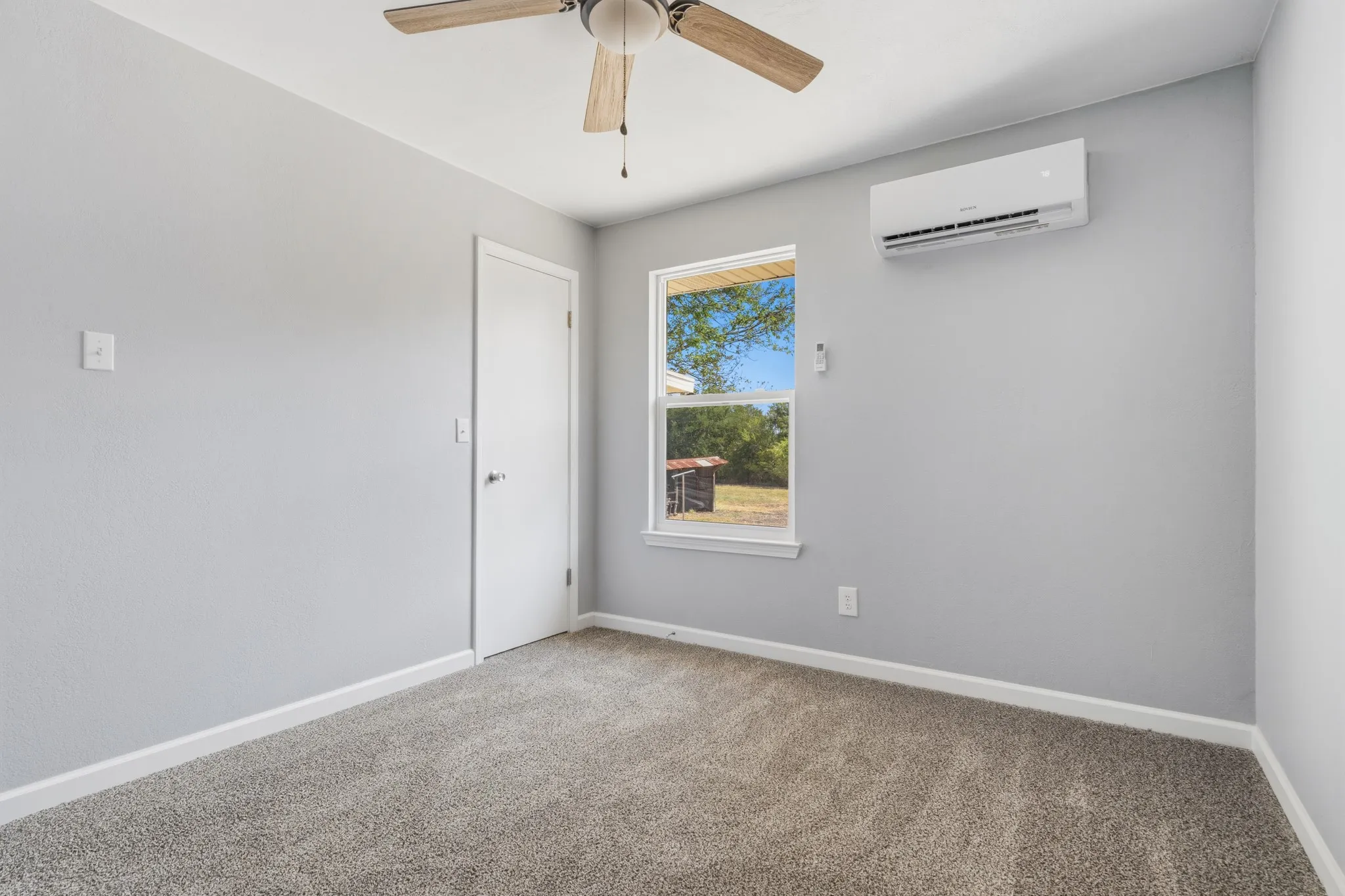 Plush gray carpet, white trim, a single window, a ceiling fan, and a wall-mounted air conditioning unit